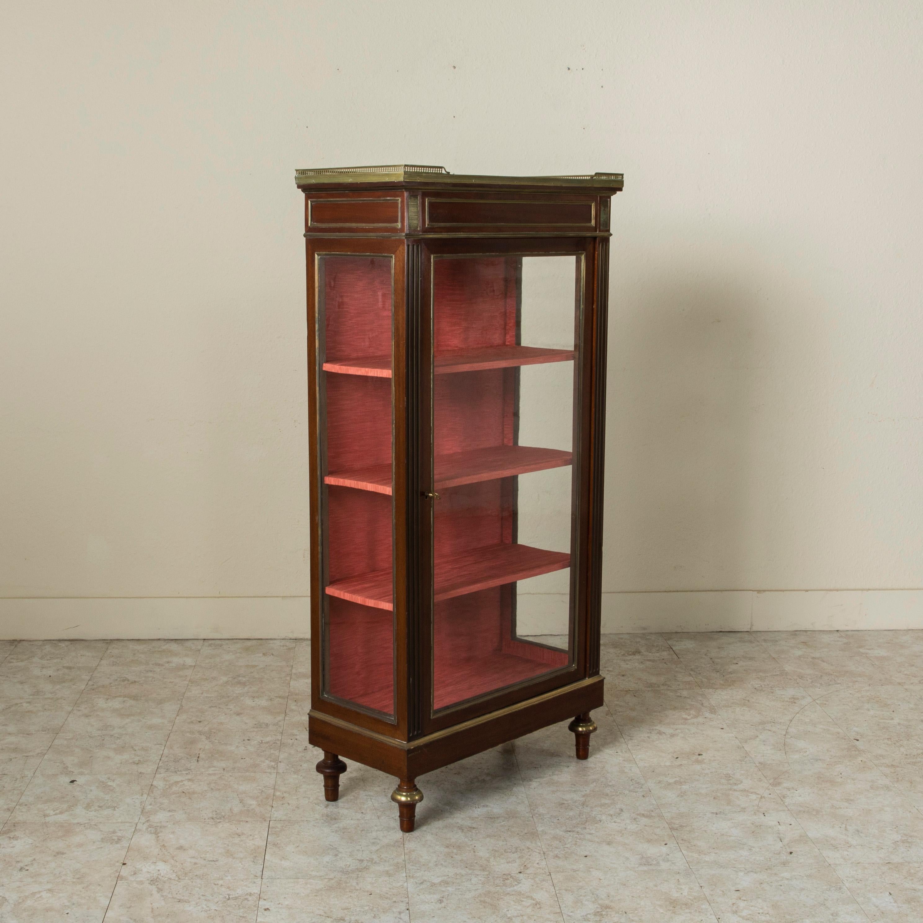 With glass on three sides, this French Louis XVI style mahogany vitrine from the late nineteenth century is ideal for displaying any fine collection. Resting on turned finial feet detailed in bronze, it also features bronze striated plaques, bronze