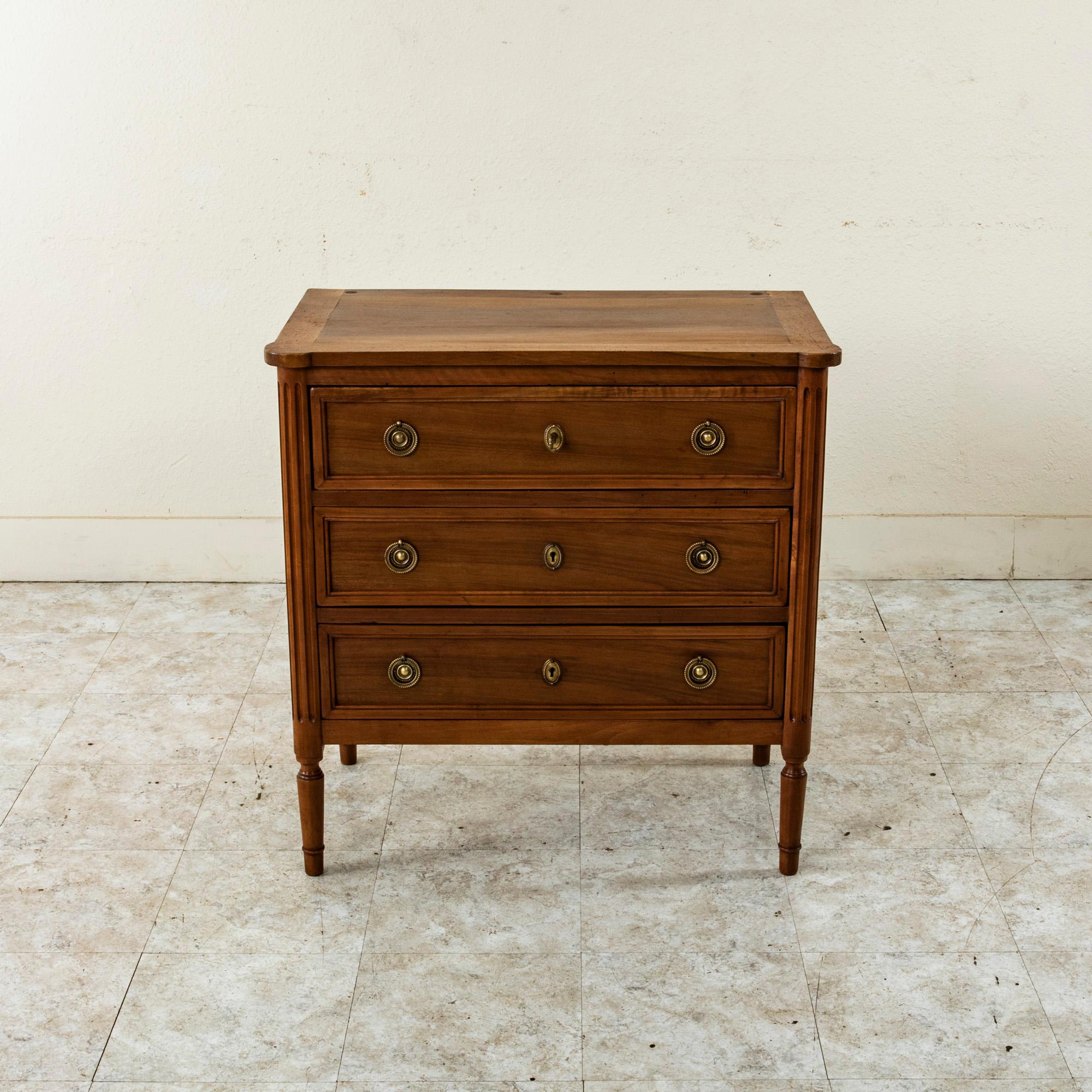 With only 31 inches in width, this small scale late nineteenth century French Louis XVI style commode or chest of drawers is constructed of solid walnut and features rounded fluted corners flanking it drawers. Its three drawers of dovetail