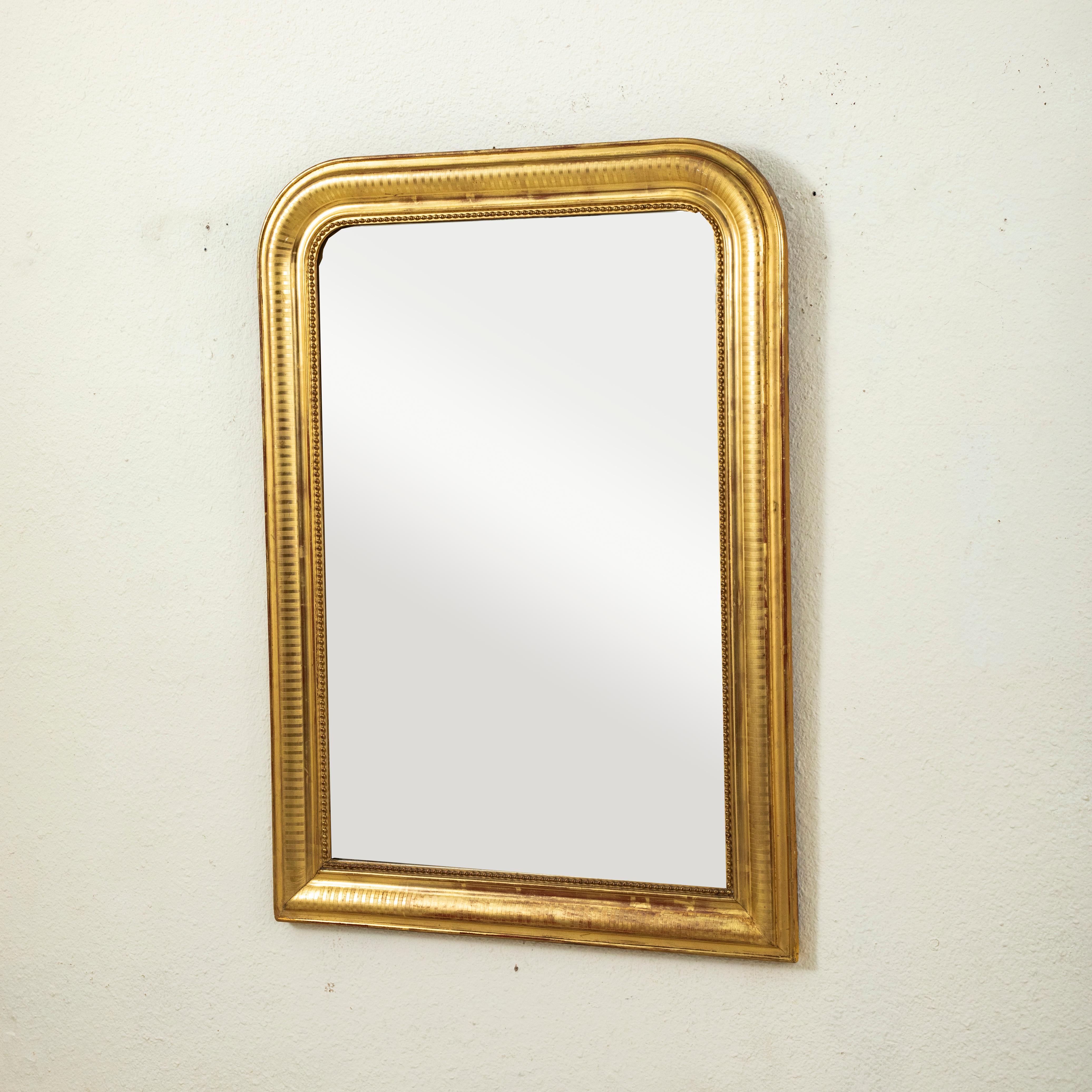 Questo specchio in legno dorato d'epoca Louis Philippe del XIX secolo presenta il suo vetro al mercurio originale. La struttura del cuscino è decorata con un sottile motivo a strisce incise e un bordo interno di perline. L'ossido di ferro originale