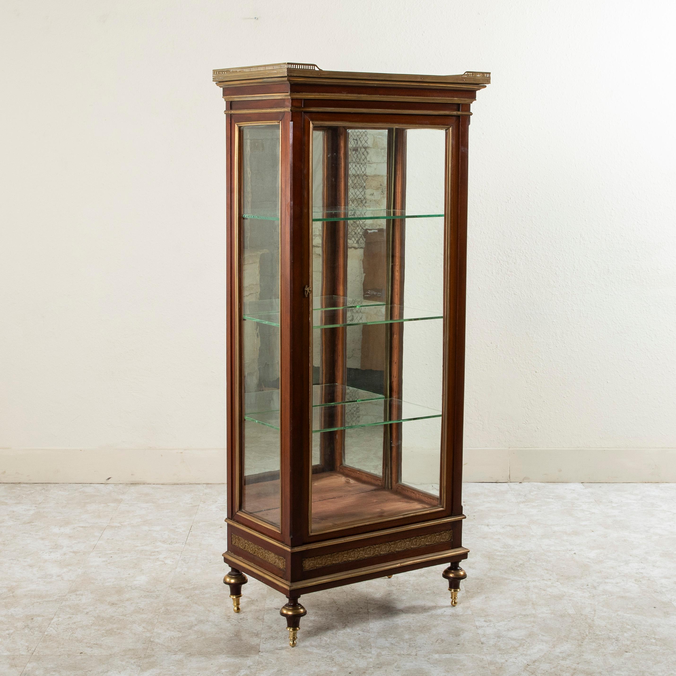 With glass on three sides, this French Louis XVI style mahogany vitrine from the mid nineteenth century is ideal for displaying any fine collection. Resting on turned finial feet detailed in bronze, this piece also features bronze detailing around