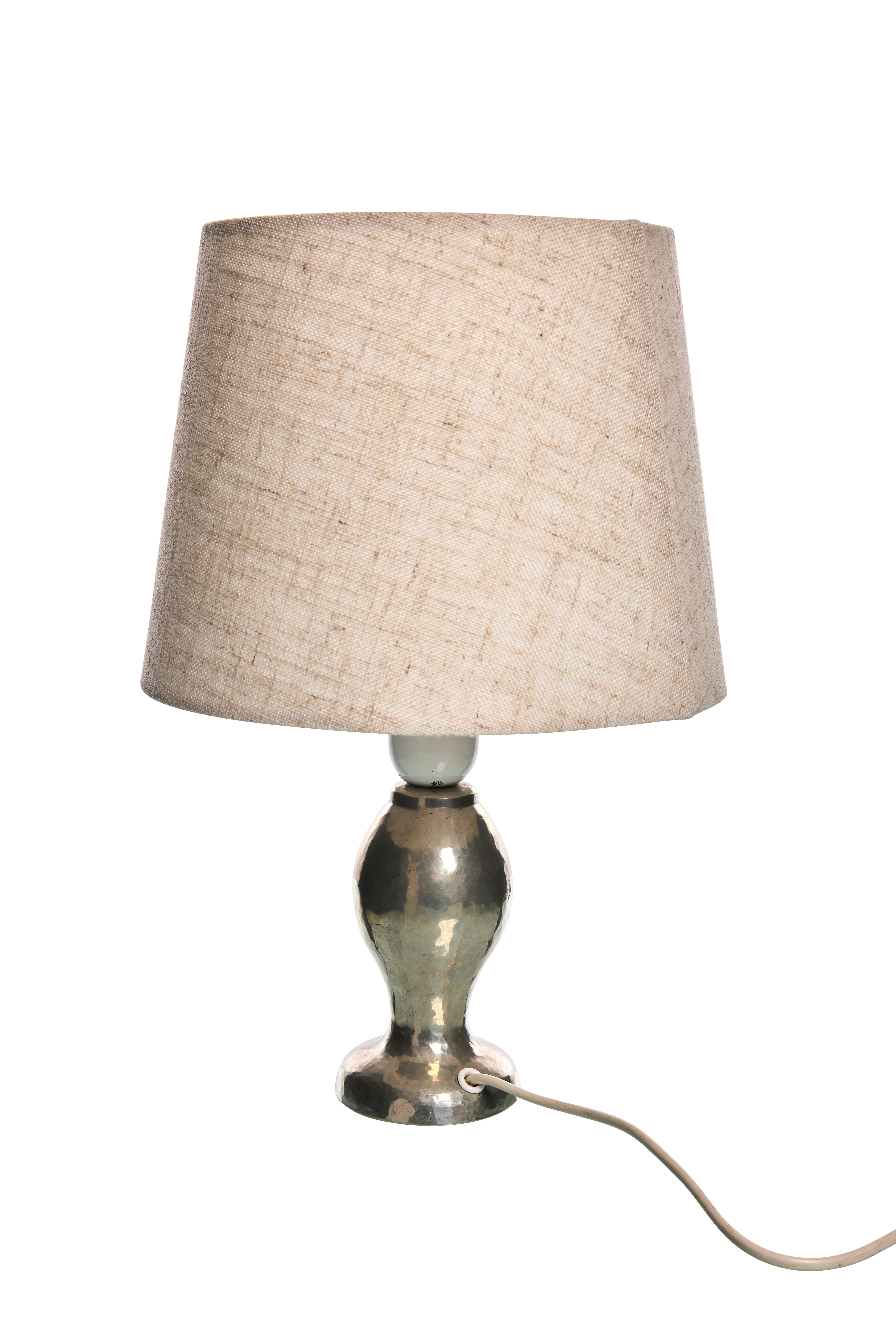 Add a touch of vintage charm to your space with this Scandinavian Modern table lamp from the 1940s. This lamp features a beautifully hand-hammered metal base that showcases a timeless, artisanal appeal. The elegant curves of the base reflect a