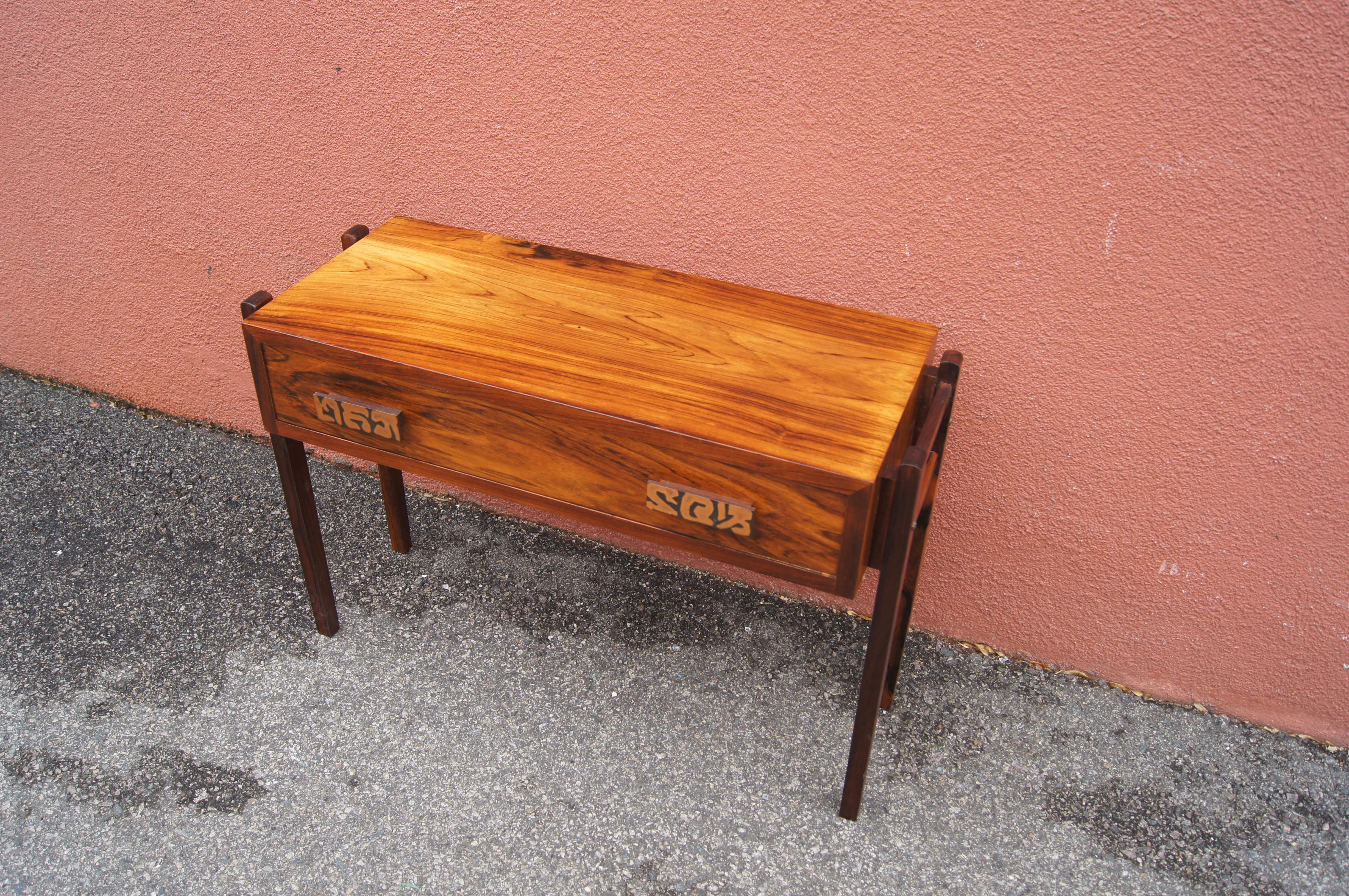 This narrow little rosewood table hangs a single-drawer case from contrasting supports. It features etched copper pulls.