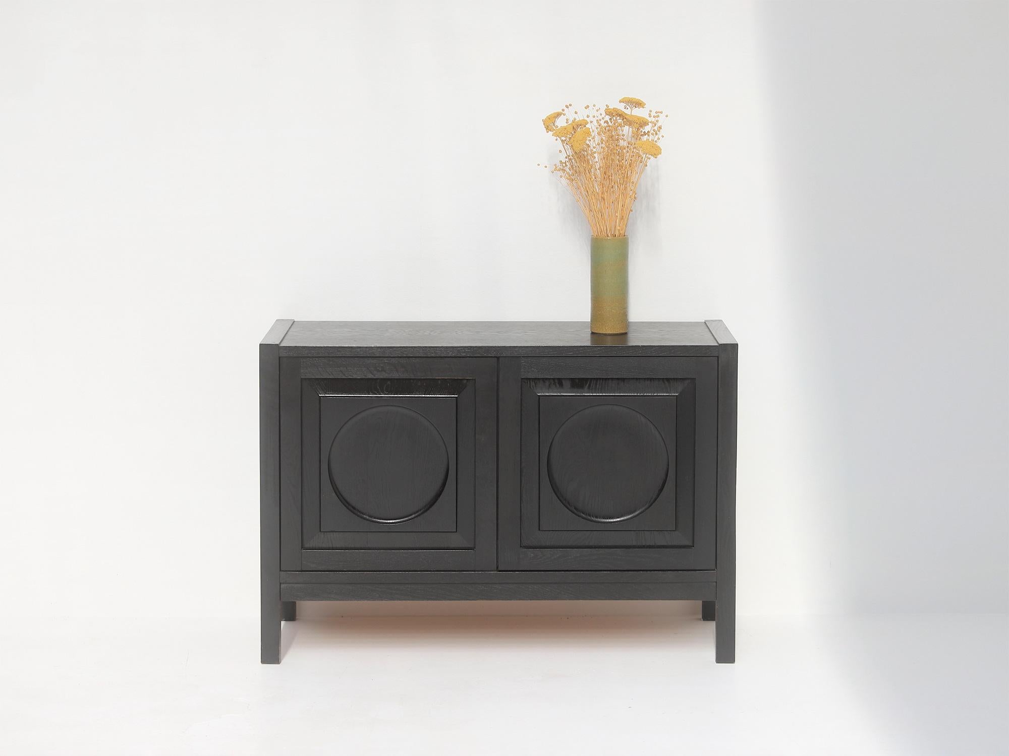 Small sideboard / cabinet produced in the 70s by Defour, Belgium. The front is decorated with a graphical circle pattern carved into the wood. The cabinet has two shelves inside. Stands in a very good and well kept condition.