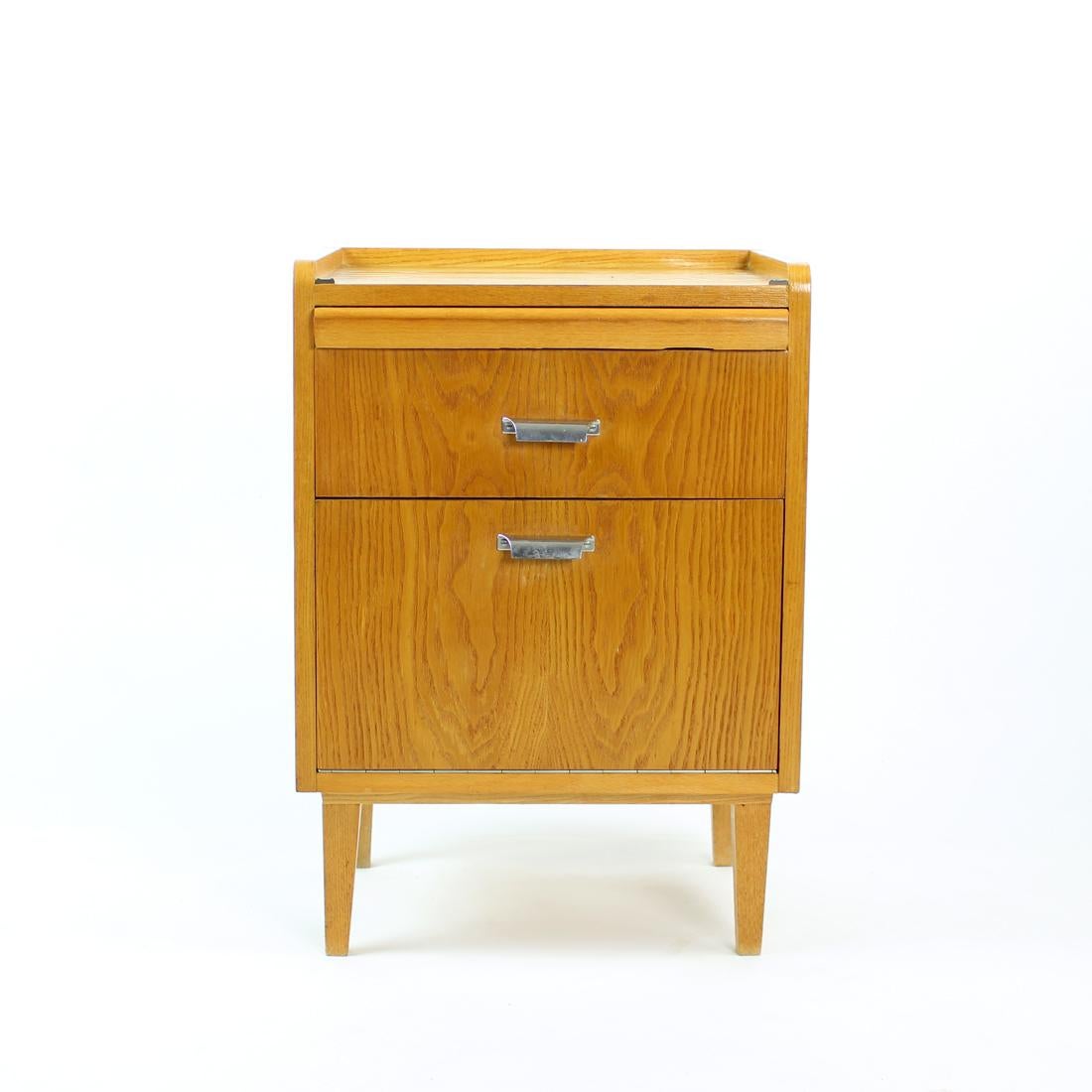 Beautiful small sideboard produced in Czechoslovakia in 1960s. The unit is in a beautiful oak wood veneer in a beautiful condition. The sideboard stands on four strong legs. There is one drawer, one compartment with doors opening on a piano hinges.