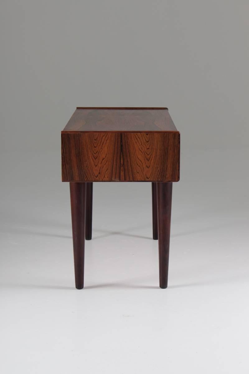 Small sideboard or end table in rosewood, with two drawers with brass handles. To show its size, we have taken a picture with a normal-sized dining chair.