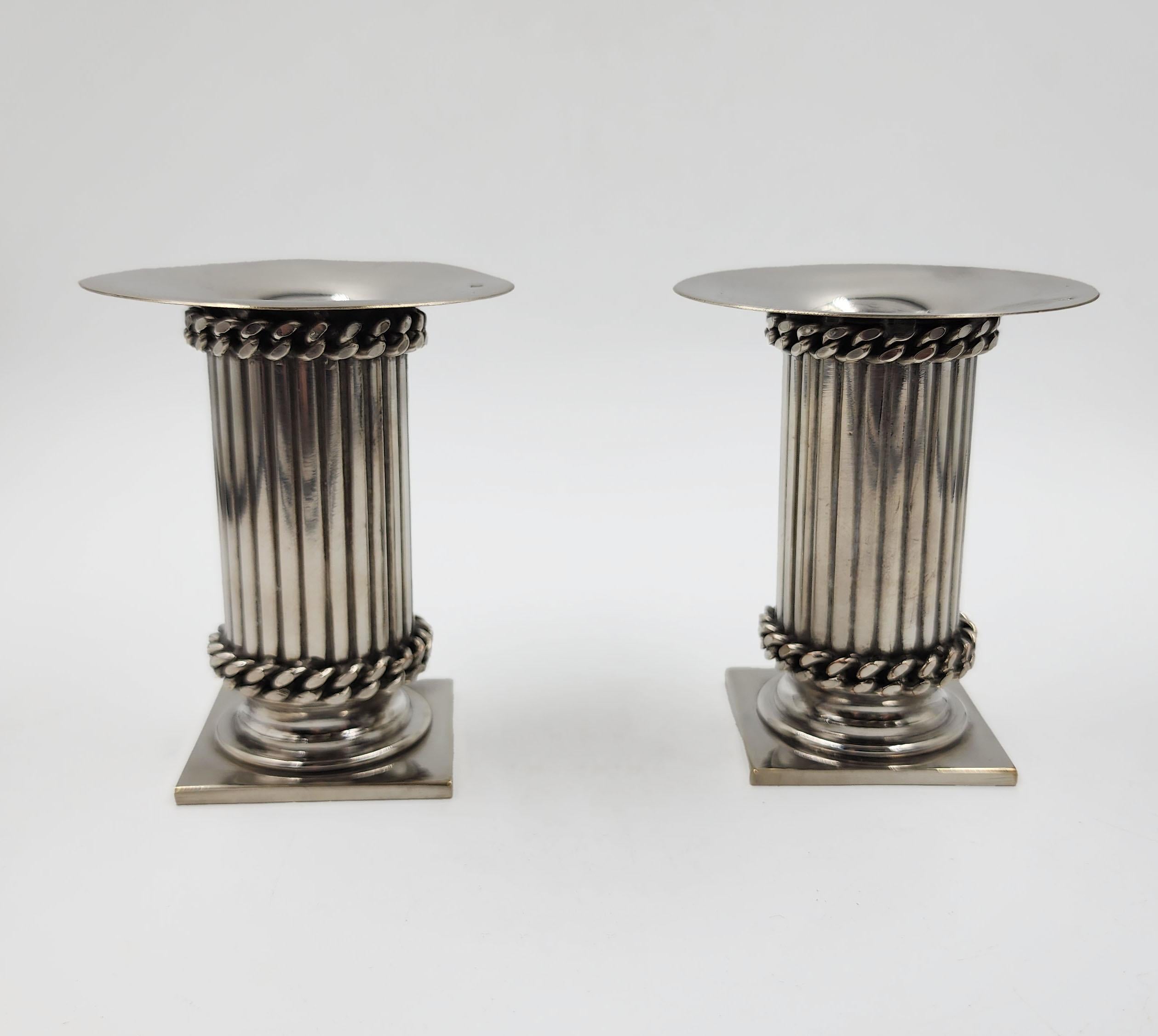 Pequeños candelabros plateados de Jean Despres
Pareja de candeleros plateados diseñados por Jean Després, con forma de columna estriada, base cuadrada y cuerpo cilíndrico. Presentan una decoración en relieve en forma de cadena en la parte superior e