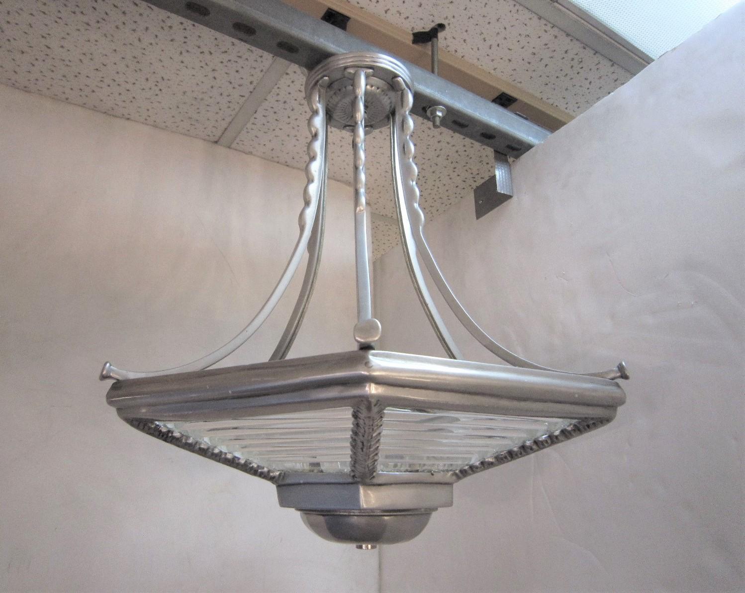 An Industrial six sided, hexagonally shaped pendant light with glass rod insets and suspended by six splay arms decorated with a lovely scalloped detail. The frame is in its natural aluminum finish
The glass may appear distorted in a few of the