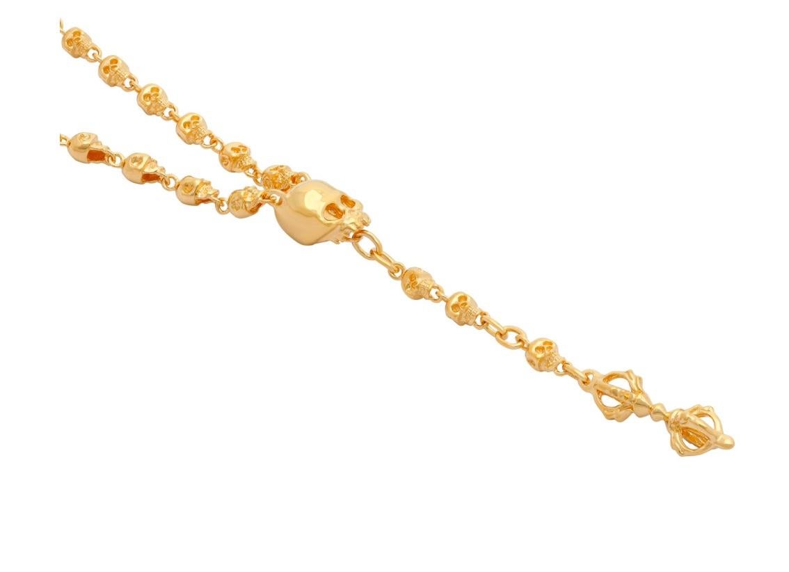 This striking piece is a Small Skull Rosary Necklace crafted in gold-plated sterling silver. The design features a delicate chain adorned with intricately detailed miniature skull beads, evenly spaced for a balanced and rhythmic aesthetic. At the