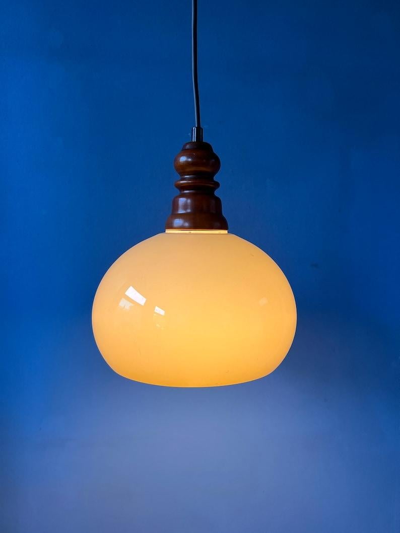Small space age pendant lamp with acrylic glass mushroom shade. The lamp has a nicely shaped wooden top cap. Experience the enchantment as the mushroom shade emits a soft and inviting glow. The delicate illumination creates an atmosphere that's