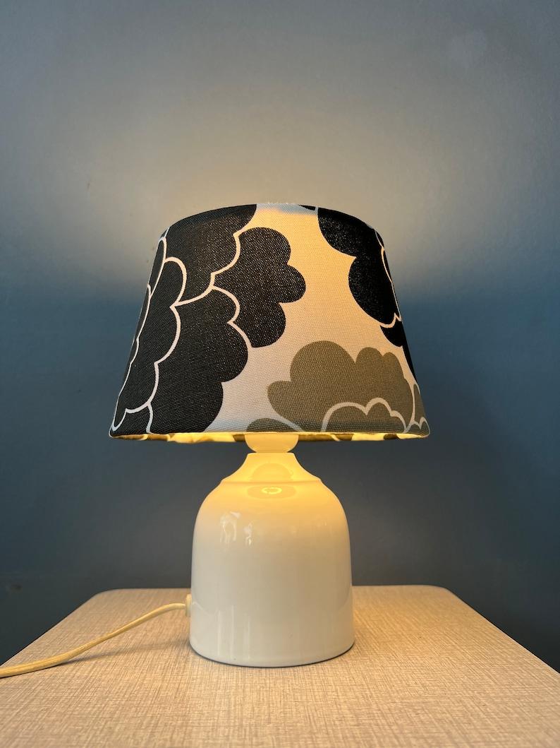 Small space age table lamp with porcelain base and hand-made black and white flower shade. The flower shade diffuses the light in a gentle and inviting manner, casting a warm and soothing ambiance that adds a touch of magic to your room. The lamp