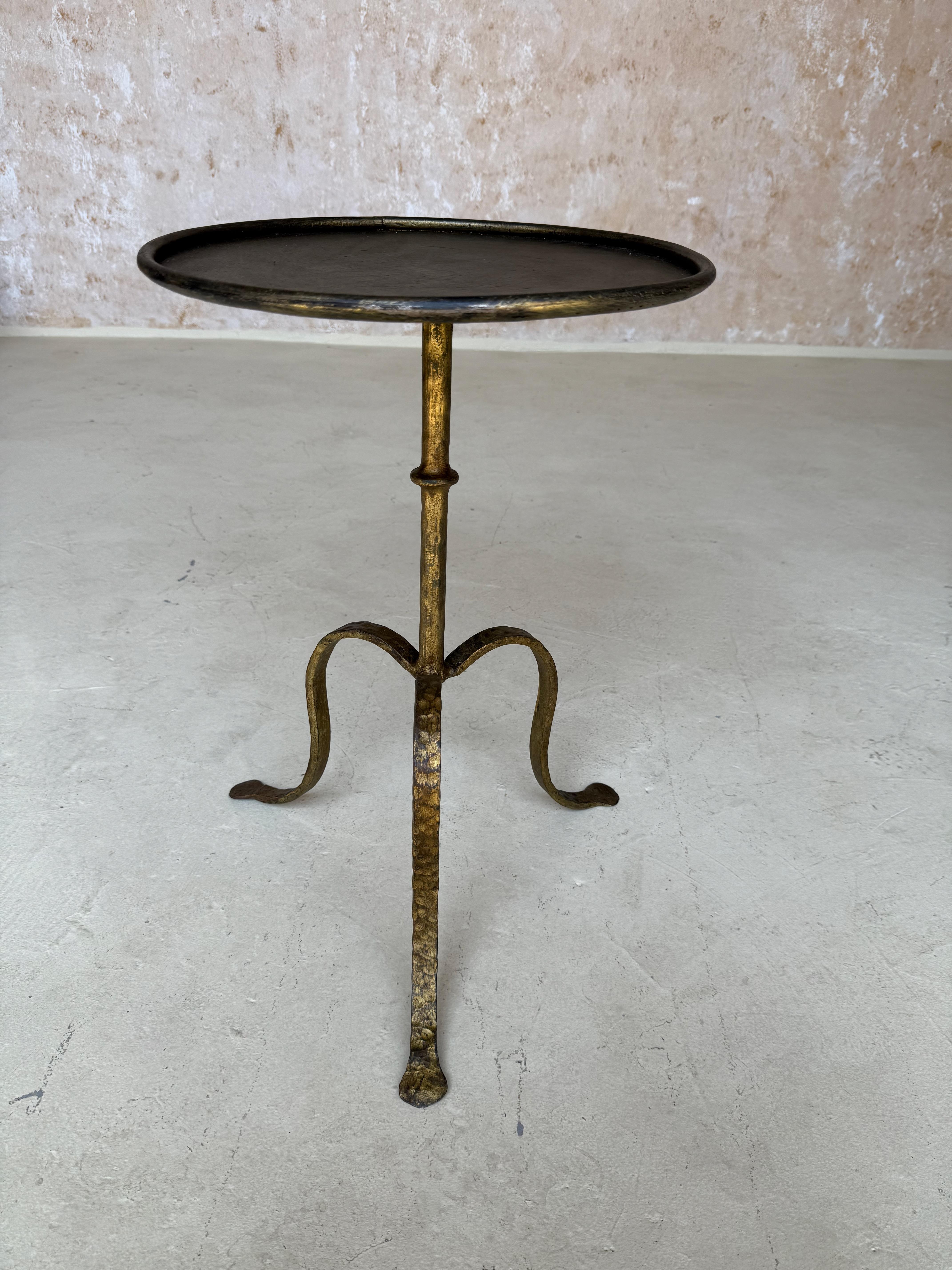 Recently handcrafted by European artisans, this refined Spanish gilt-iron drinks table features a slender stem with ring detail and a graceful arched tripod base. The round top with raised rim and hand-applied gilt finish reveal a warm, aged patina.