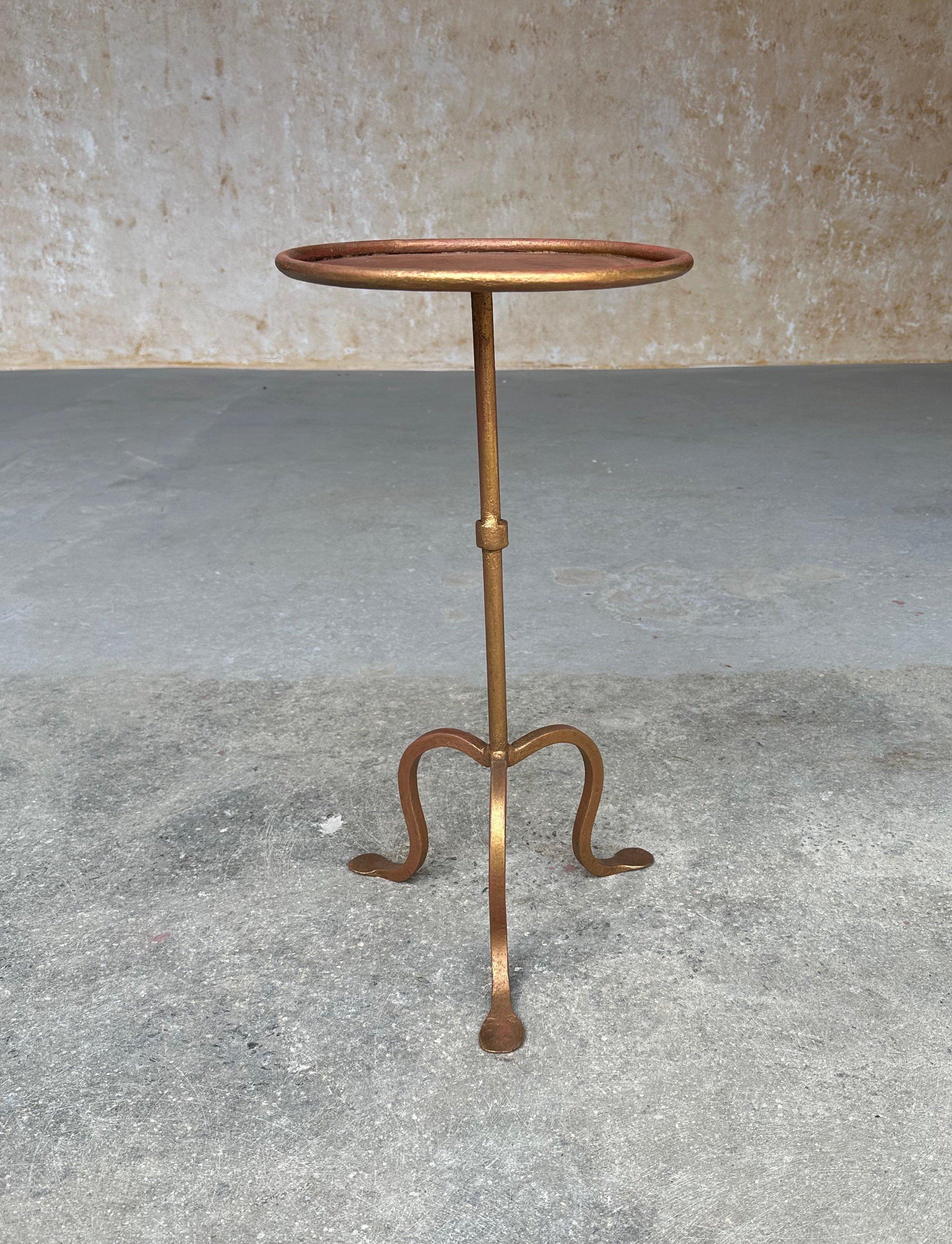 This lovely Spanish iron drinks table was recently crafted by skilled artisans and features a hand-applied gilt gold finish with red undertones. The stem has a central ring detail and is mounted on a sturdy tripod base with gracefully flared legs,