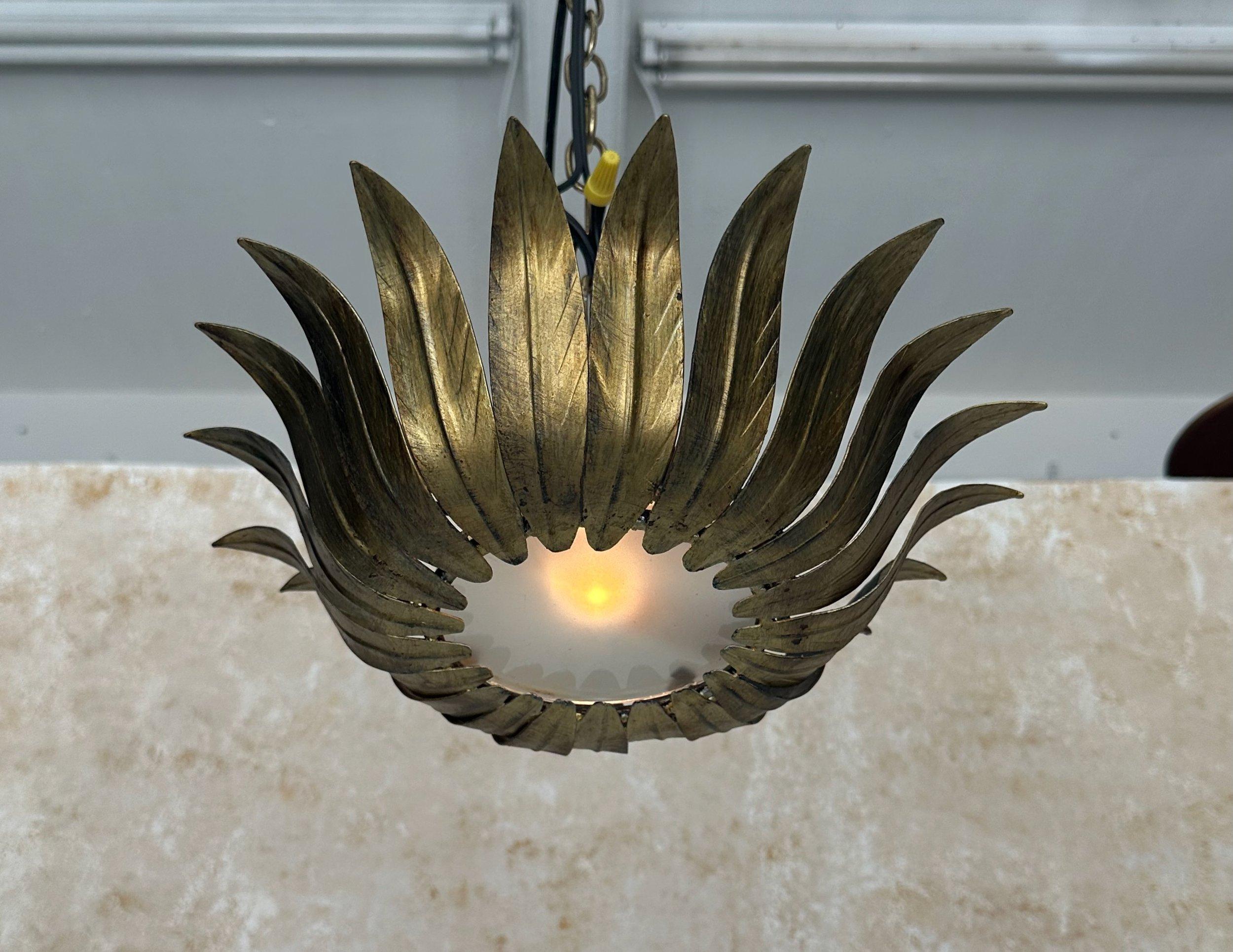 This unique small scale 1950s Spanish gilt metal ceiling fixture features evenly spaced leaves that frame the circular frosted glass center and curve dramatically upwards. The original hand applied gilt finish gives this piece vintage charm and it