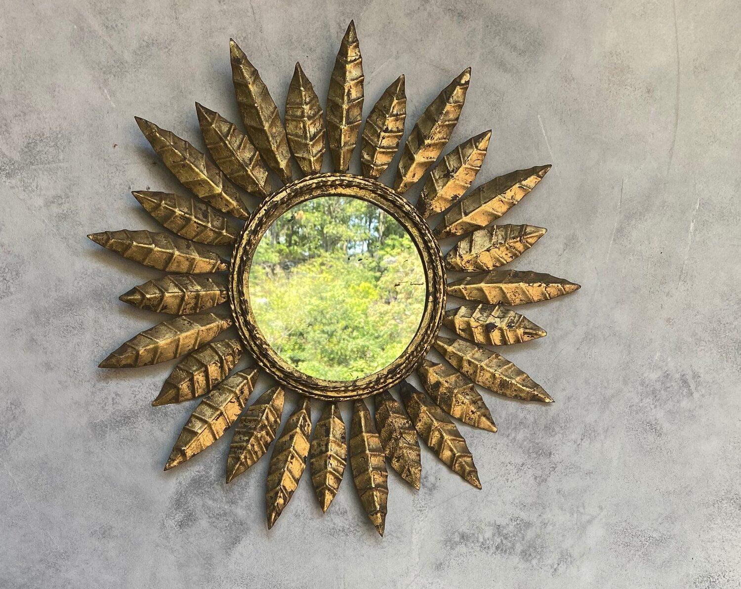 This striking Spanish sunburst mirror, dating back to the 1950s, features a gilt metal frame with a unique design of alternating leaf motifs that radiate from a twisted rope detail. The mirror has been recently updated with a new felt backing,