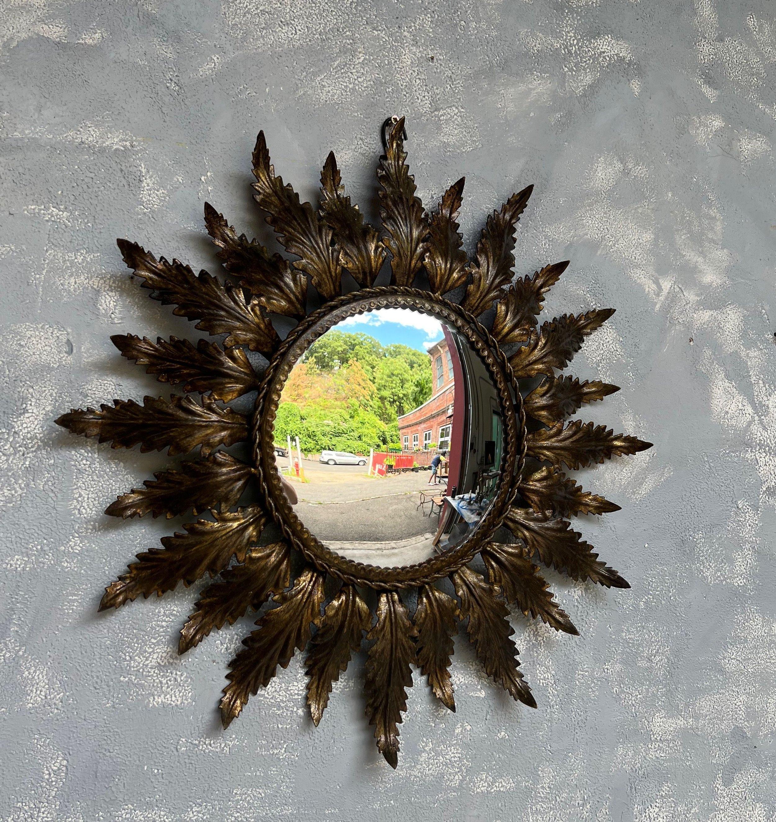 A small Spanish 1950s round gilt metal sunburst mirror. This mid-century round gilt metal sunburst mirror is a gem. It features radiating leaves surrounding a convex mirror with a braided frame, adding an element of dimensionality and complexity to
