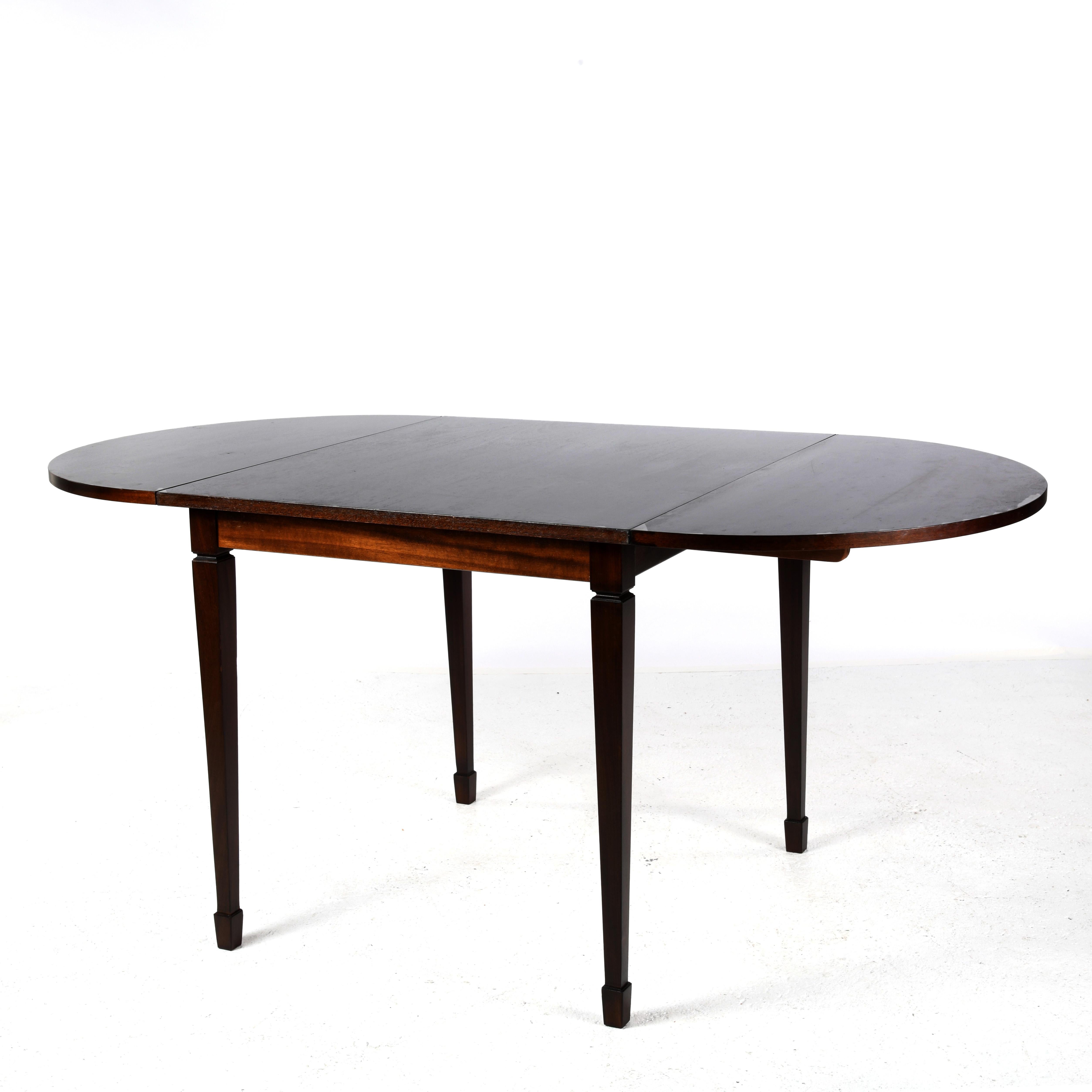 Small square table in stained wood from Denmark. Two removable semi-circular leaves can be folded down to form an oval table. They can be folded away to the sides or removed completely. Tapered legs finished with shoes. Sliders under the central