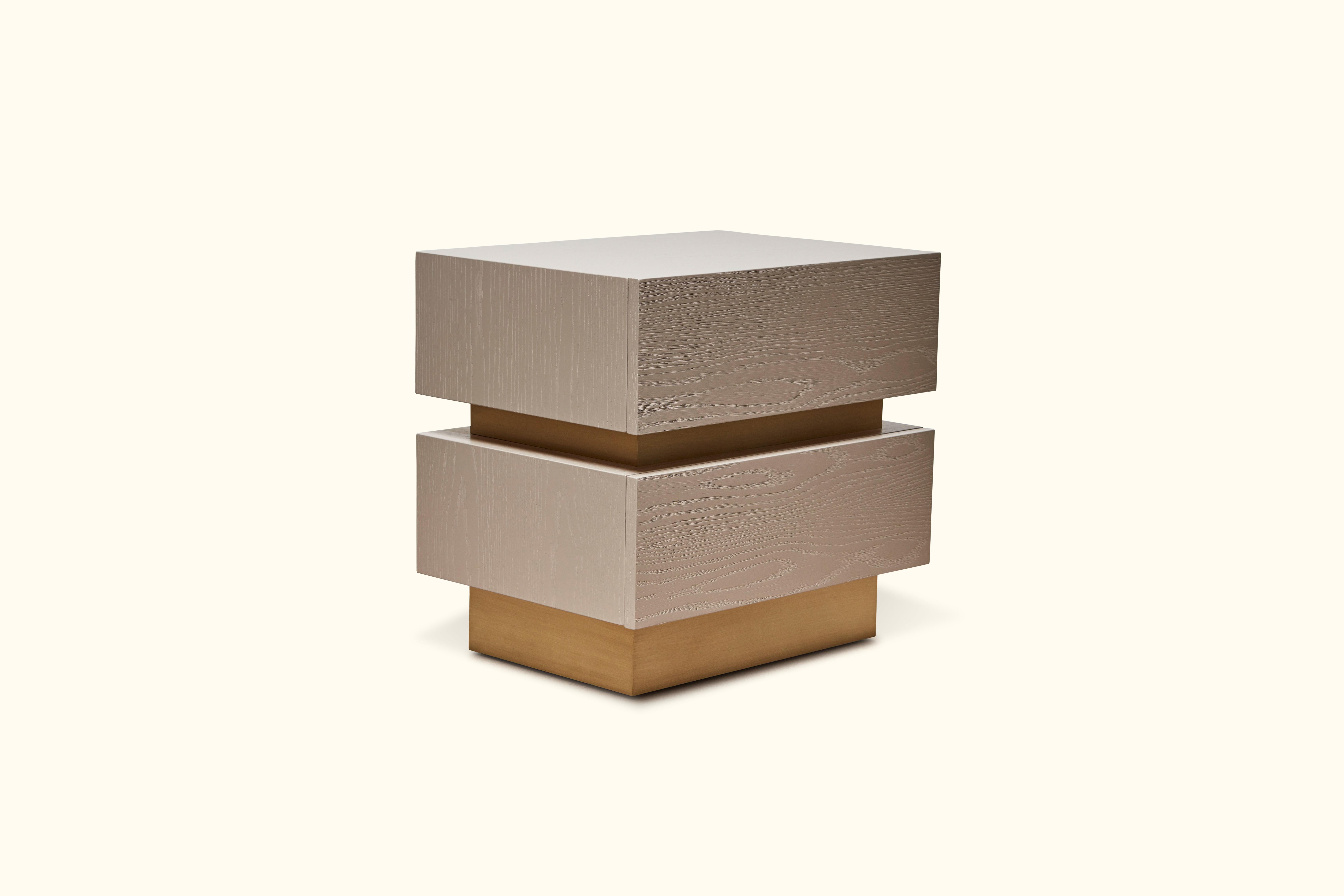 The stacked box nightstand with brass inset is a bedside table with two drawers that is available in various finishes of American walnut, or white oak and features a brass inset detail between the drawers. Show here in rocky beach pigmented oak and