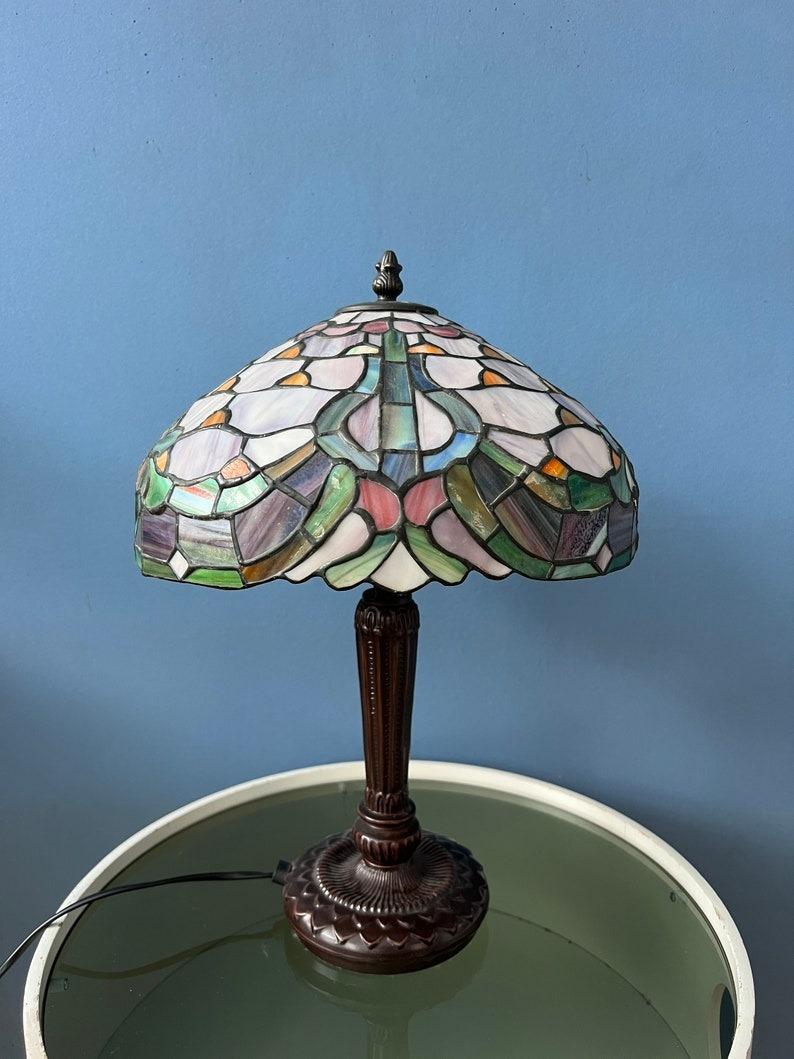 Big Tiffany desk lamp with very colourful patterned stained glass shade. The base is made out of metal and the shade is made from acrylic. The stained glass produces a warm light effect. The shade can be taken off the base and positioned in any way