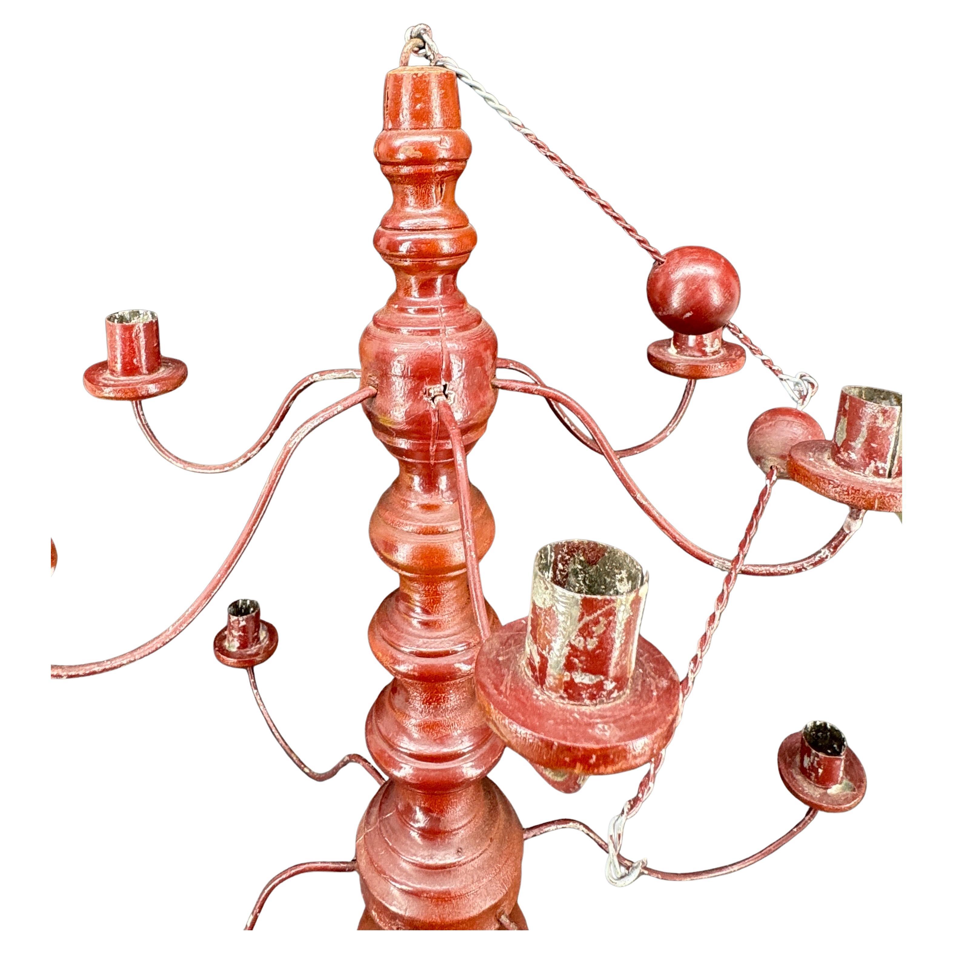 A charming Swedish folk art candle chandelier in turned wood with a rusty red painted finish. 12 metal arms support the wood candle holders. As illustrated in Milieu Magazine (Winter 2025 page 32-34), this chandelier would be a great bright light