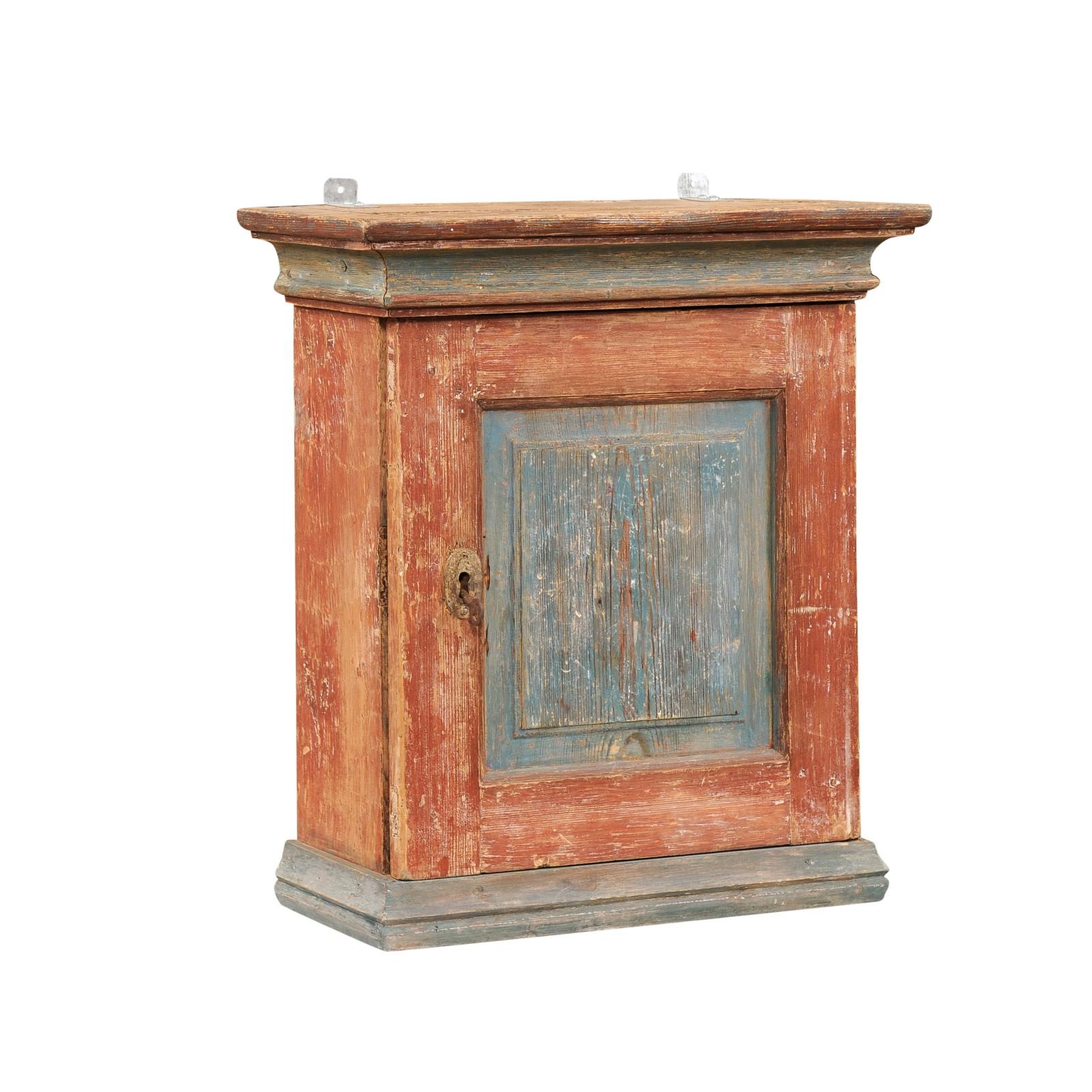 A Swedish rustic small wall hanging cabinet from the 19th century, with polychrome finish, single door and nicely weathered patina. Capturing our attention with its small proportions and great rustic charm, this small Swedish wall hanging cabinet