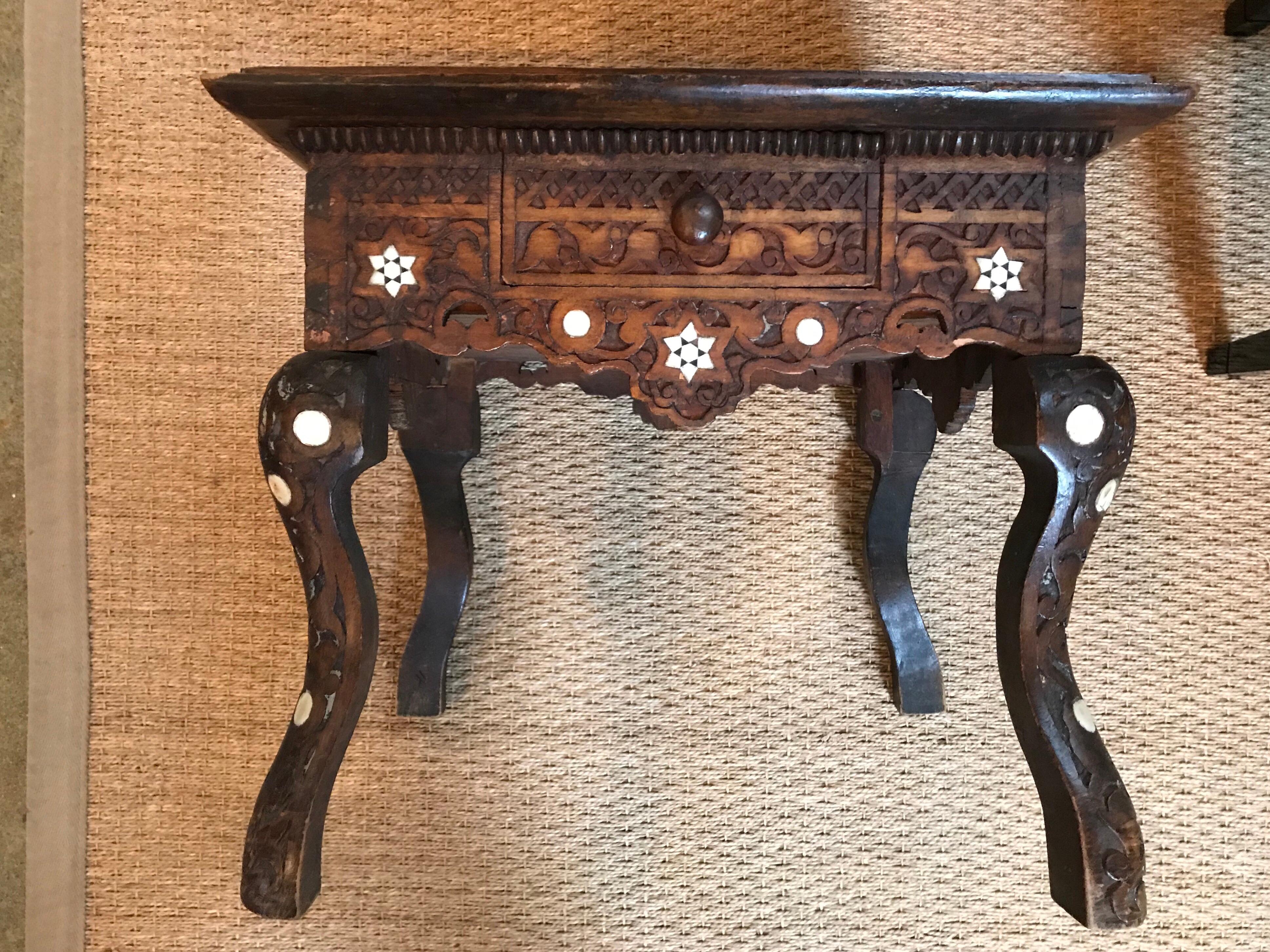 This small, Syrian inlaid dark wooden table has a single drawer, a square top, with cabriole legs and is ornately decorated.