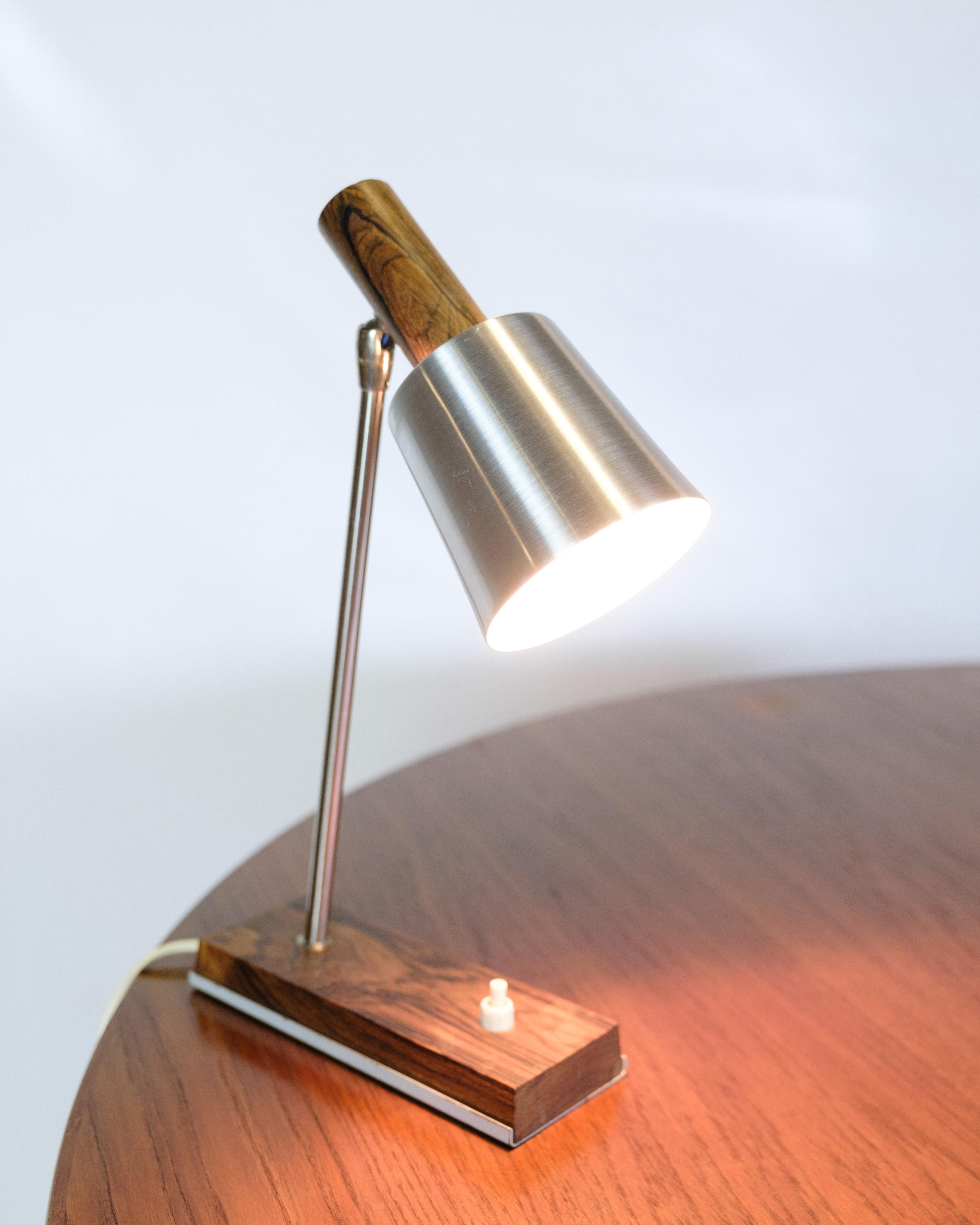 Piccola lampada da tavolo, modello Silva, disegnata per Lyfa negli anni '60. Realizzata con una base in palissandro, un'asta in acciaio spazzolato e un paralume in alluminio, con eleganti dettagli in legno sulla testa della lampada. La lampada ha un
