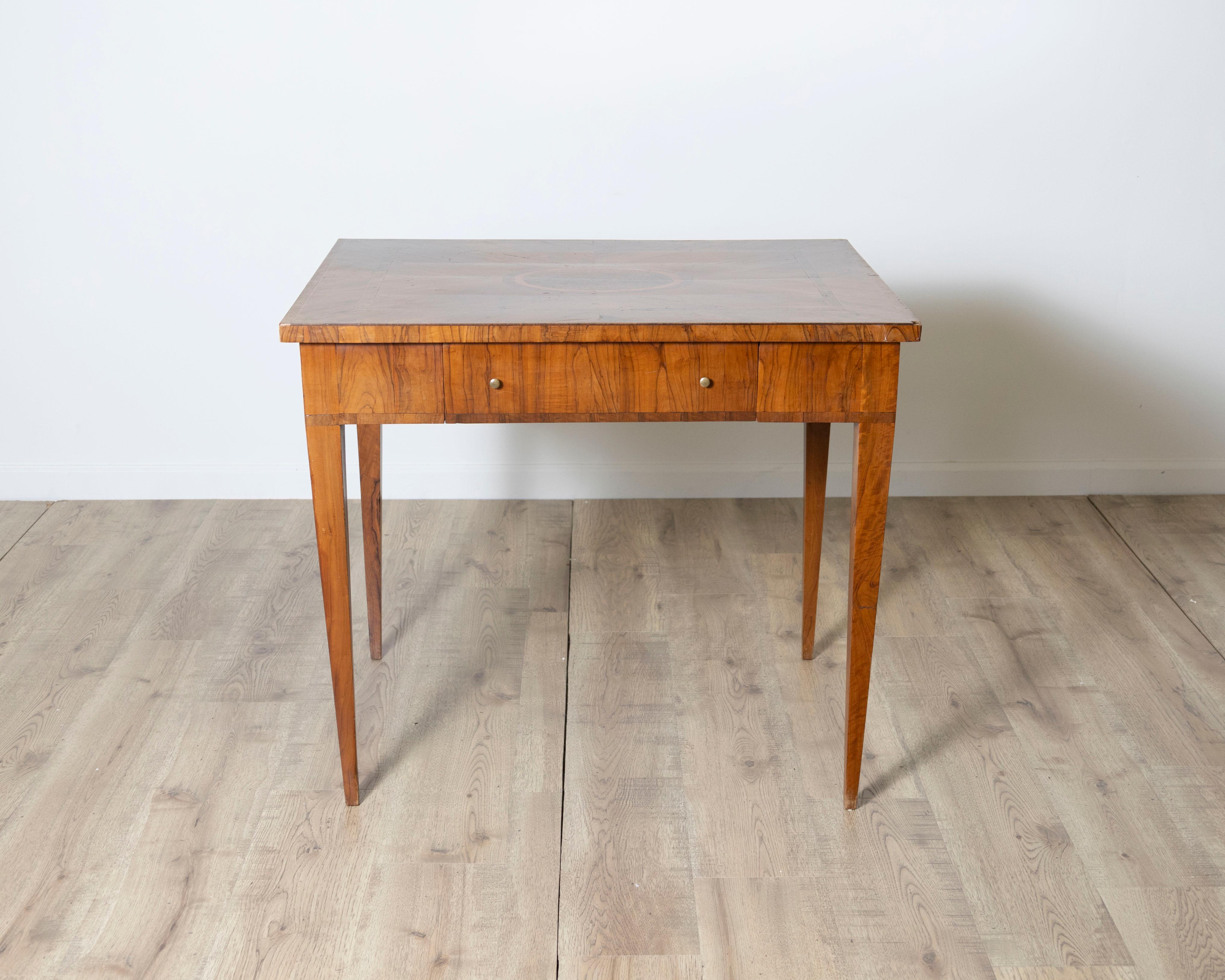 Un raffinato tavolino toscano della fine del XVIII secolo, splendidamente impiallacciato in legno d'ulivo e intarsiato con vari legni a contrasto per creare una composizione geometrica di grande effetto.

Il piano quadrato è centrato da un