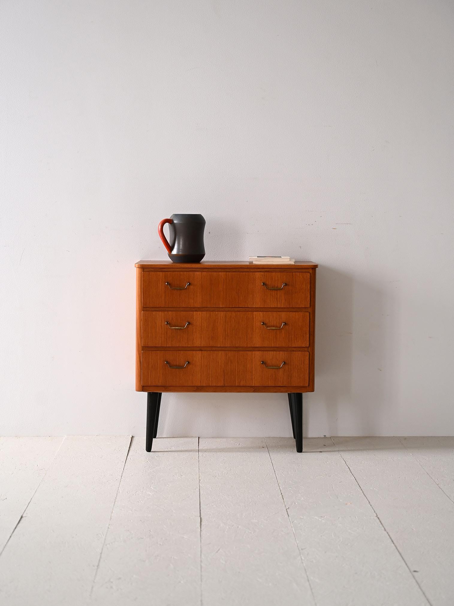Scandinavian furniture from the 1960s with black painted legs.

An original, small chest of drawers also ideal as a bedside table. It is distinguished by the gilded metal handles on the drawers and the conical wooden legs painted black.
The modern