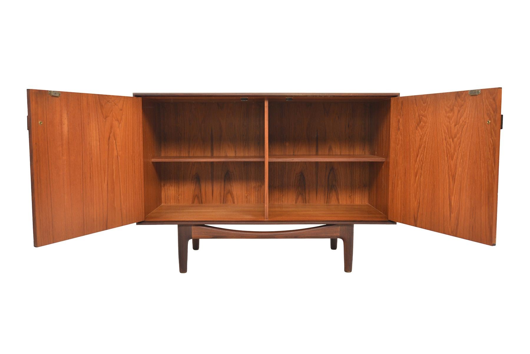 This small mid century teak credenza was designed by Ib Kofod Larsen for G Plan in 1961 for the Danish Range. Crafted in teak and afrormosia with handsomely refined lines, two wide doors open to reveal two bays with adjustable shelving. Finished on