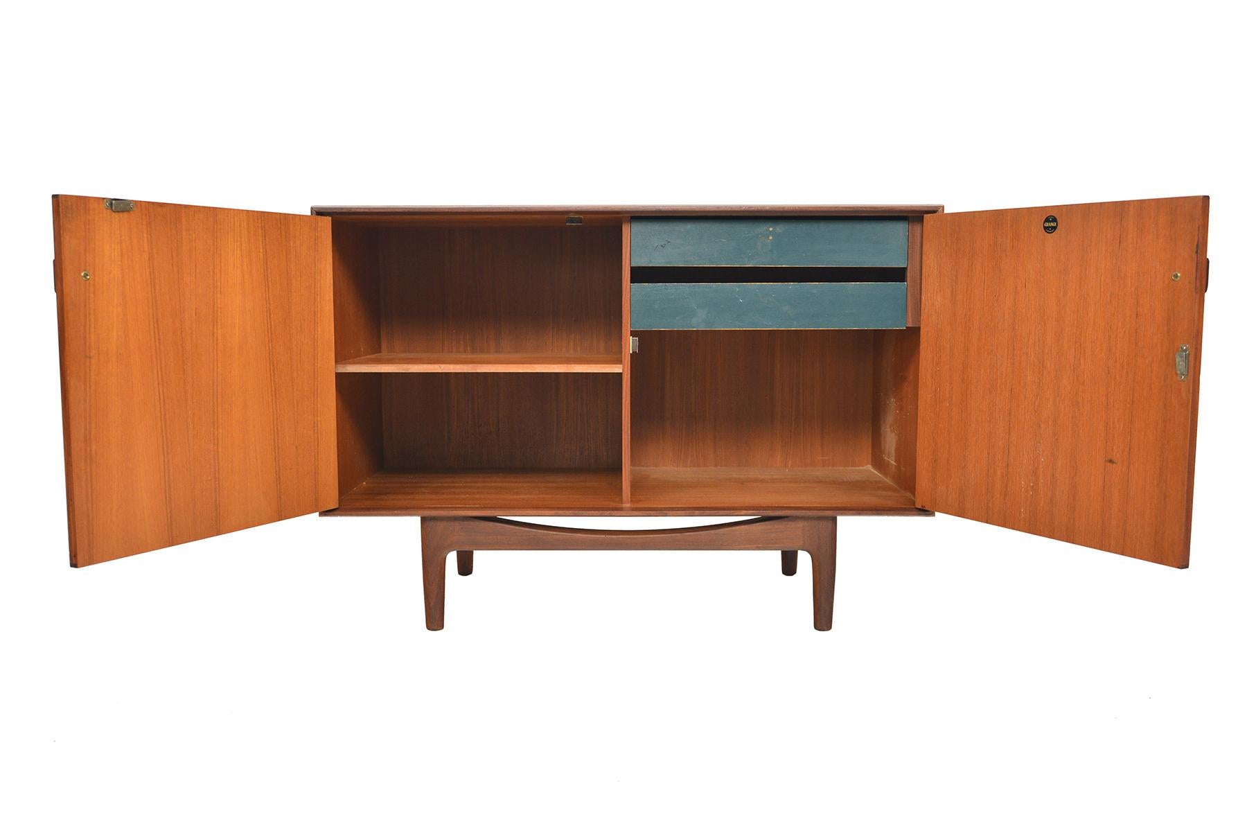 This small mid century teak credenza was designed by Ib Kofod Larsen for G Plan in 1961 for the Danish Range. Crafted in teak and afrormosia with handsomely refined lines, two wide doors open to reveal two bays an adjustable shelf and two drawers.