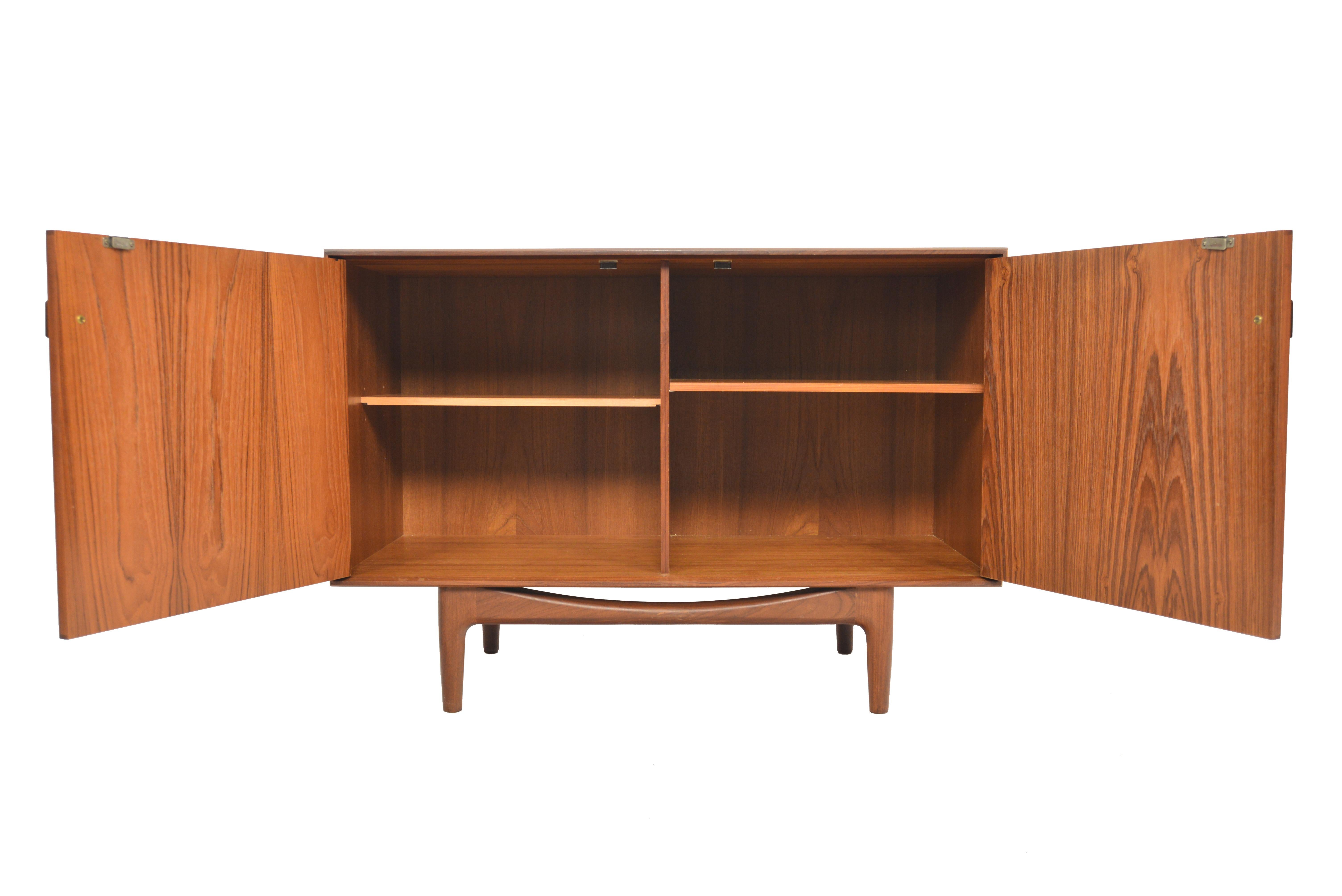 This small midcentury teak credenza was designed by Ib Kofod Larsen for G Plan in 1961 for the Danish Range. Crafted in teak and afrormosia with handsomely refined lines, two wide doors open to reveal two bays with adjustable shelving. Finished on