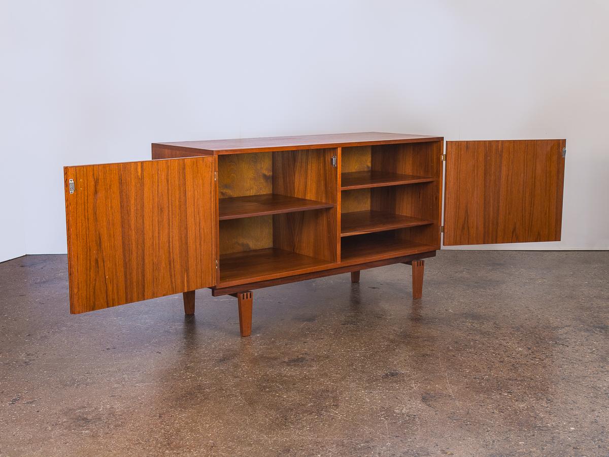 Elegant teak sideboard by Peter Lovig Nielsen. A beautiful example of 1960s Danish modern cabinetry. The teak wood has been polished and is gleaming with a striking grain. The two hinged doors feature pretty brass hardware details, and hand-carved