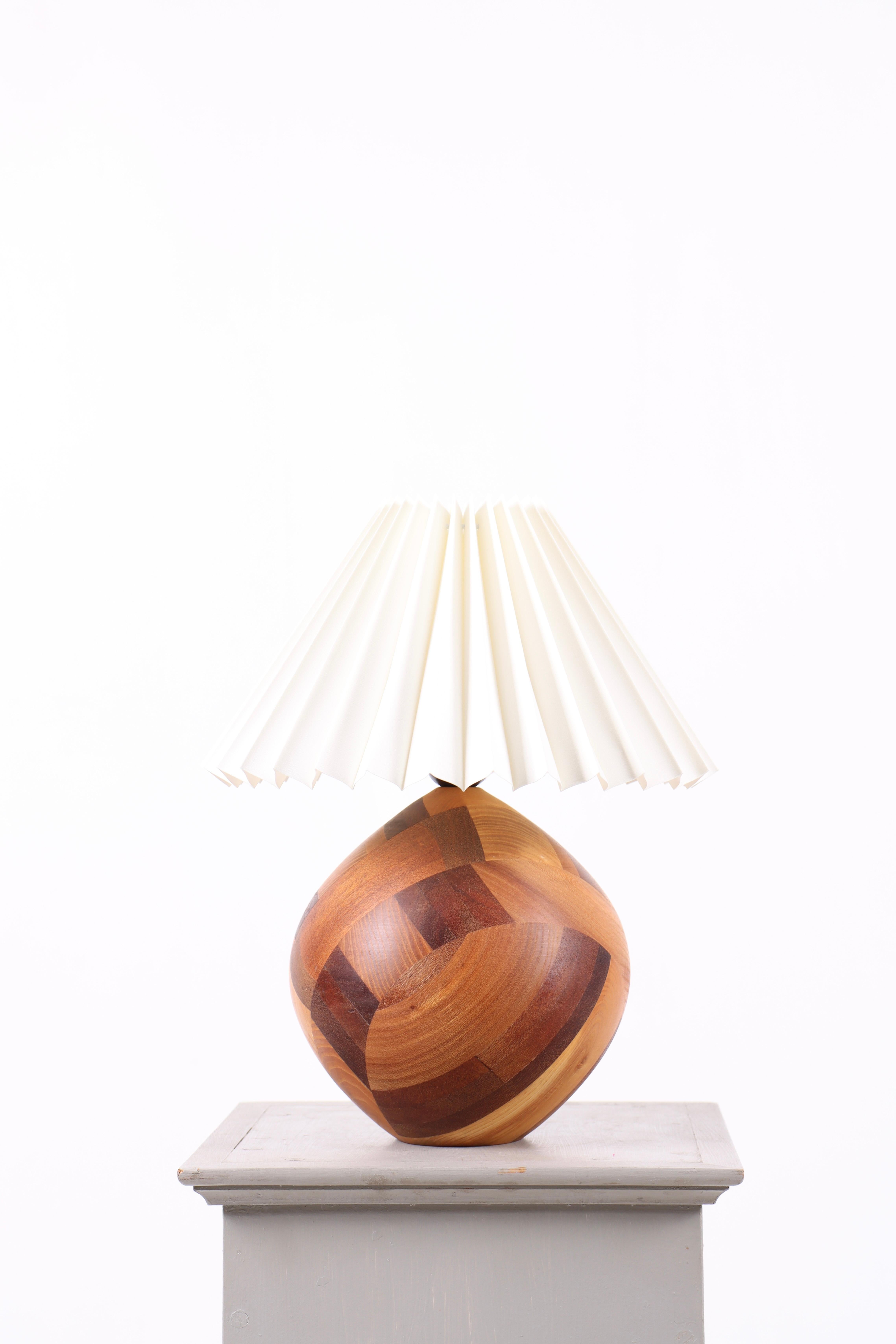 Decorative table lamp crafted in solid teak with a geometric pattern of assembled wood pieces, creating a warm and vibrant surface. The lamp is fitted with a new, classic pleated shade that adds a light and timeless expression.
Produced in Denmark