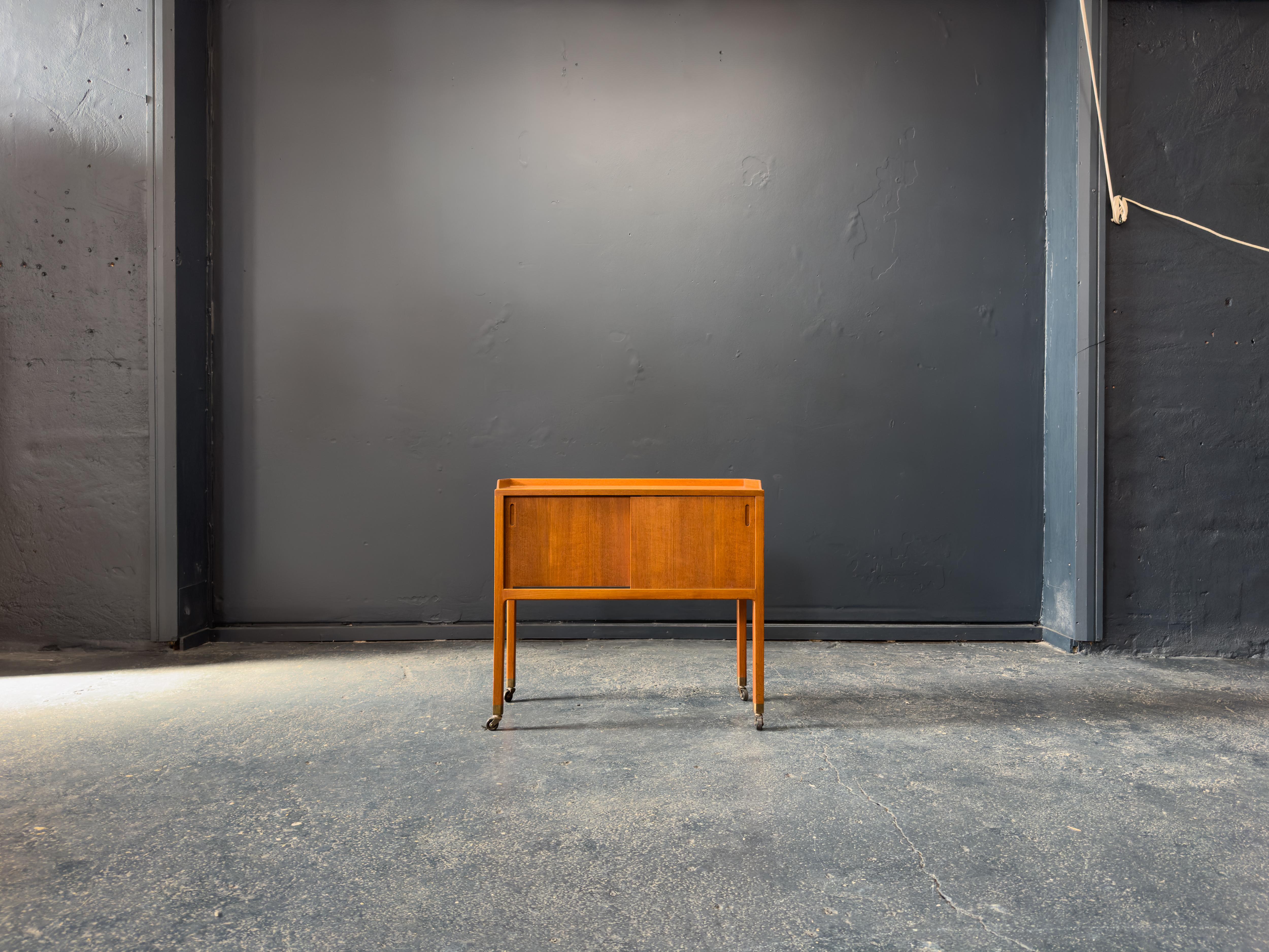 Questa raffinata credenza compatta in teak è un pezzo forte del design danese di metà secolo, che offre fascino visivo e praticità in un ingombro ridotto. Realizzato in teak con un'ottima lavorazione, il mobile presenta una venatura calda e color