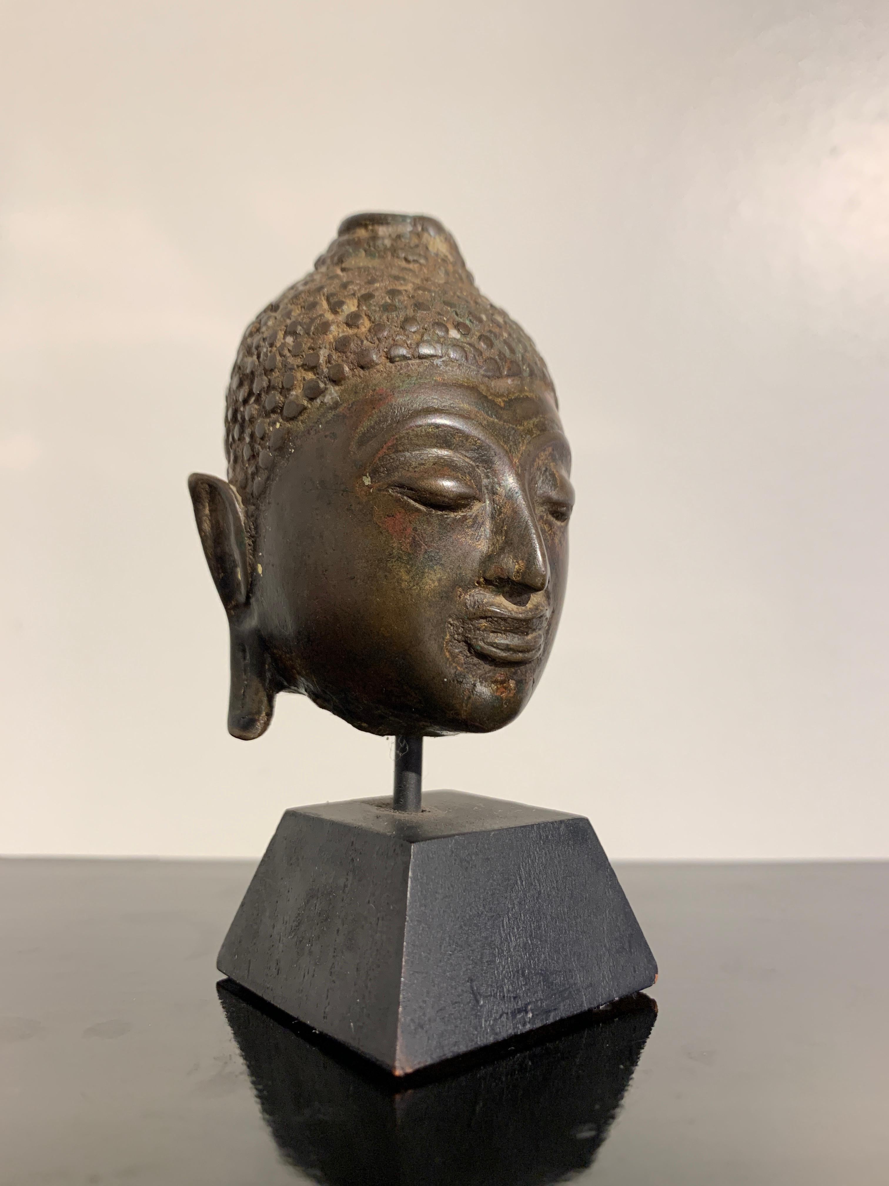 A small and charming fragmentary cast bronze Buddha head with traces of gilding and lacquer, Lan Na Kingdom, Chiang Saen style, 16th century, Thailand.

The small head of the Buddha from the ancient kingdom of Lan Na, with typical Chiang Saen