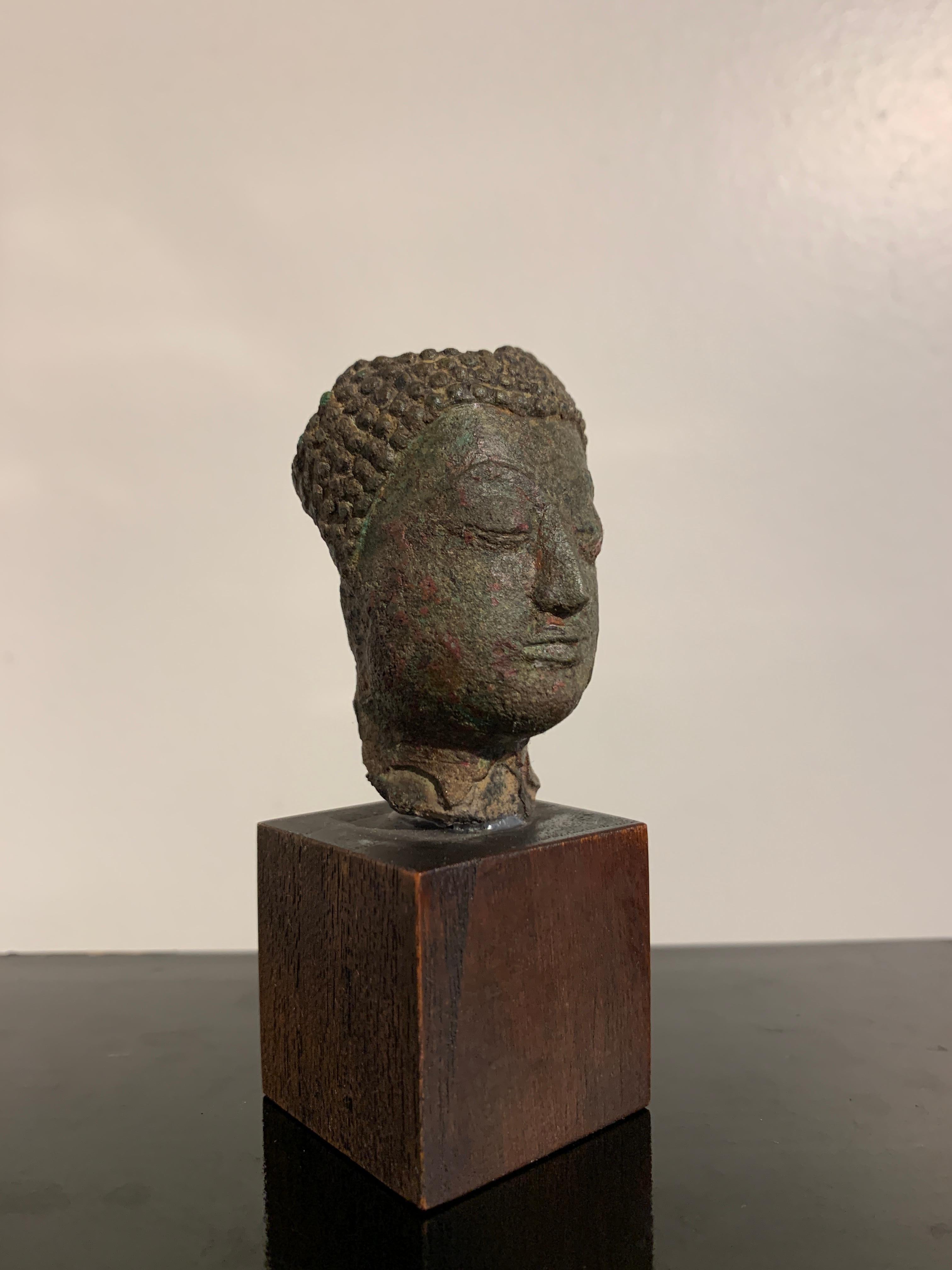 A small mounted Thai bronze Buddha head, late Sukhothai period, style of Kamphaeng Phet, 14th-15th century, Thailand.

The small Buddha head fragmentary, and originally part of a larger figure. The head with typical features of the Kamphaeng Phet
