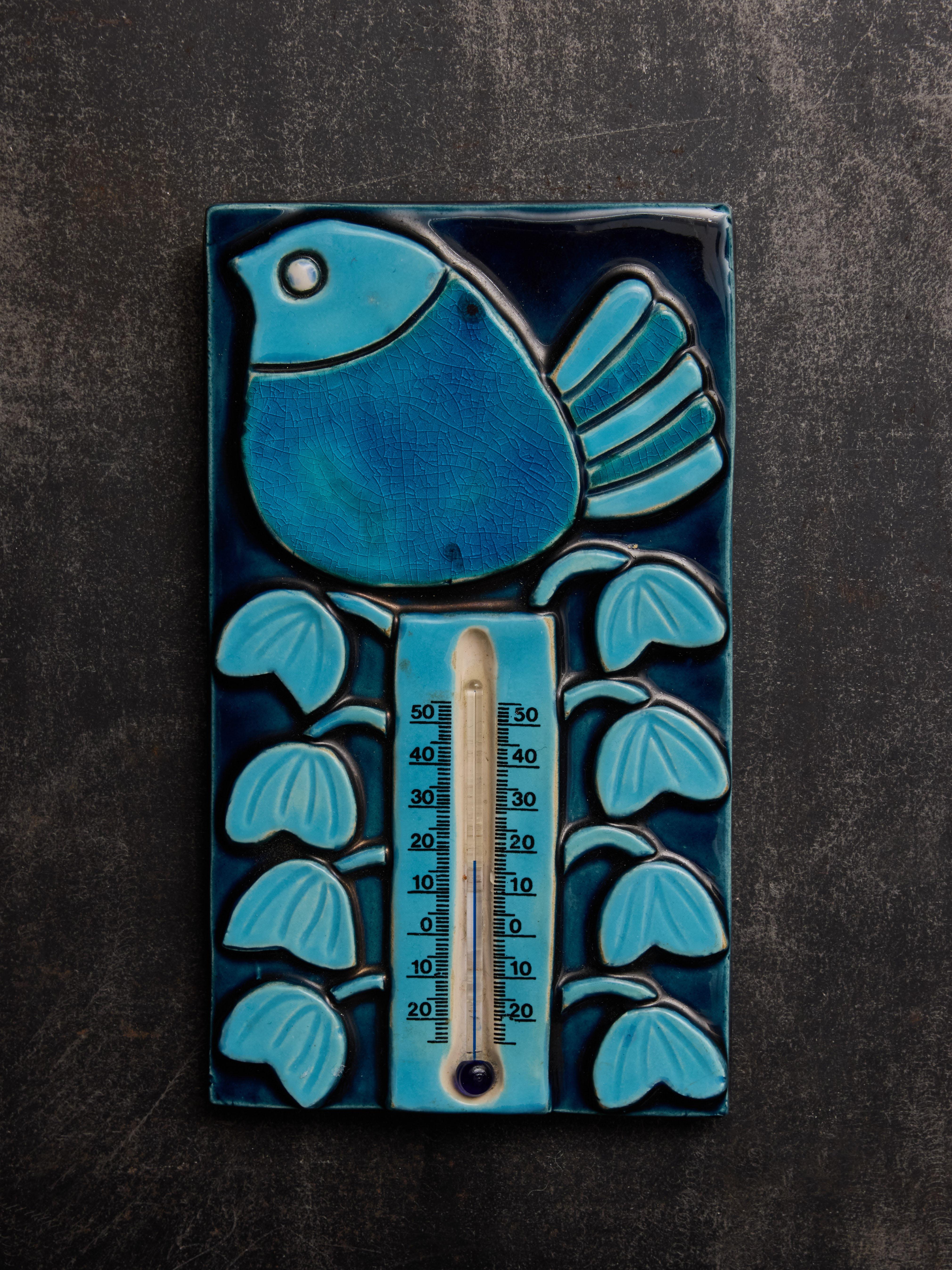 Charming ceramic wall thermometer by Mithé Espelt, adorned with floral designs and a prominent bird, all showcased in various shades of blue glaze.

A small decorative thermometer made by Mithé Espelt, featuring a rectangular glazed ceramic frame