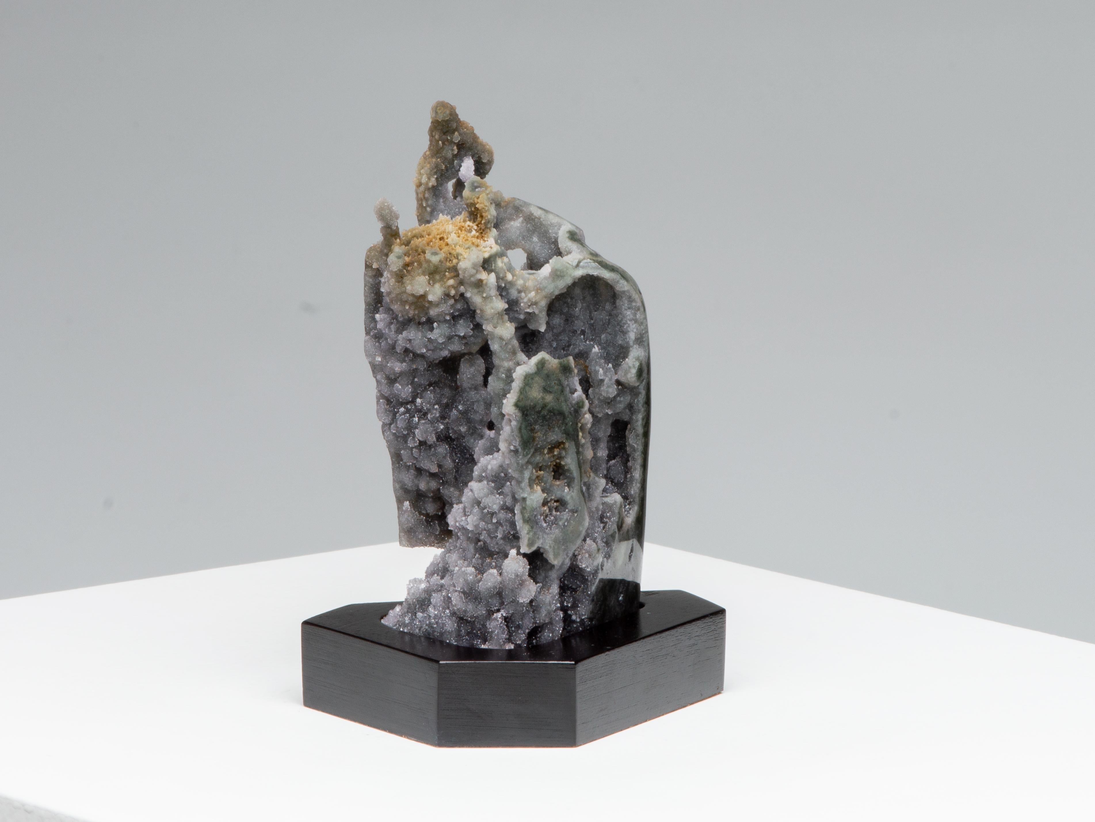 This small towering stalactite formation is covered in grey druze with tanbrown
accents and transparent quartz overlaying green celadonite.

This piece was legally and ethically sourced directly in the prestigious mines of Uruguay, South America.