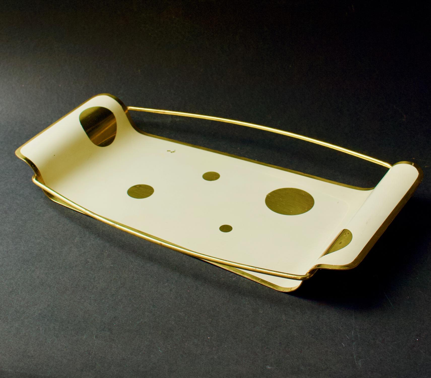 A small tray of painted brass, mid-20th century Germany.

The tray is of asymmetrical shape, with curved ends and long side rails. The top is painted in creamy off-white to reveal circles of brass and a brass edge. An attractive piece, possibly