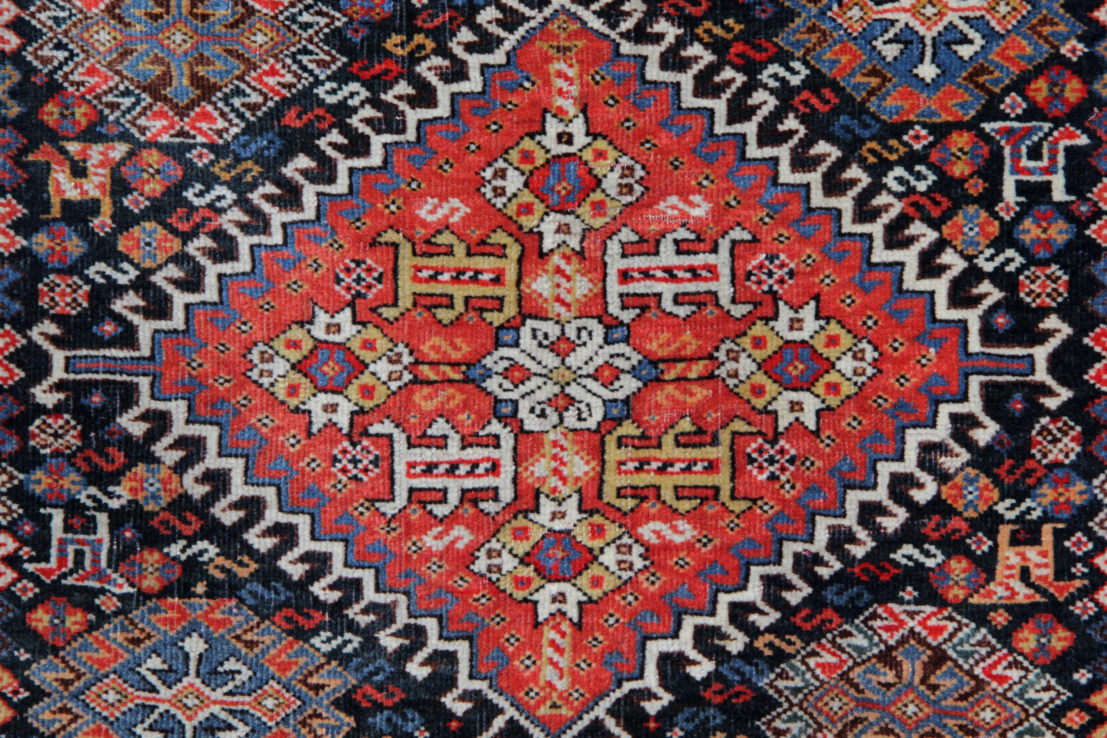 This beautiful oriental rug features a red field with a unique central medallion, the diamond is then surrounded by smaller motifs and animal figures woven on a contrasting black background in accents of red, ivory and blue. The border is highly