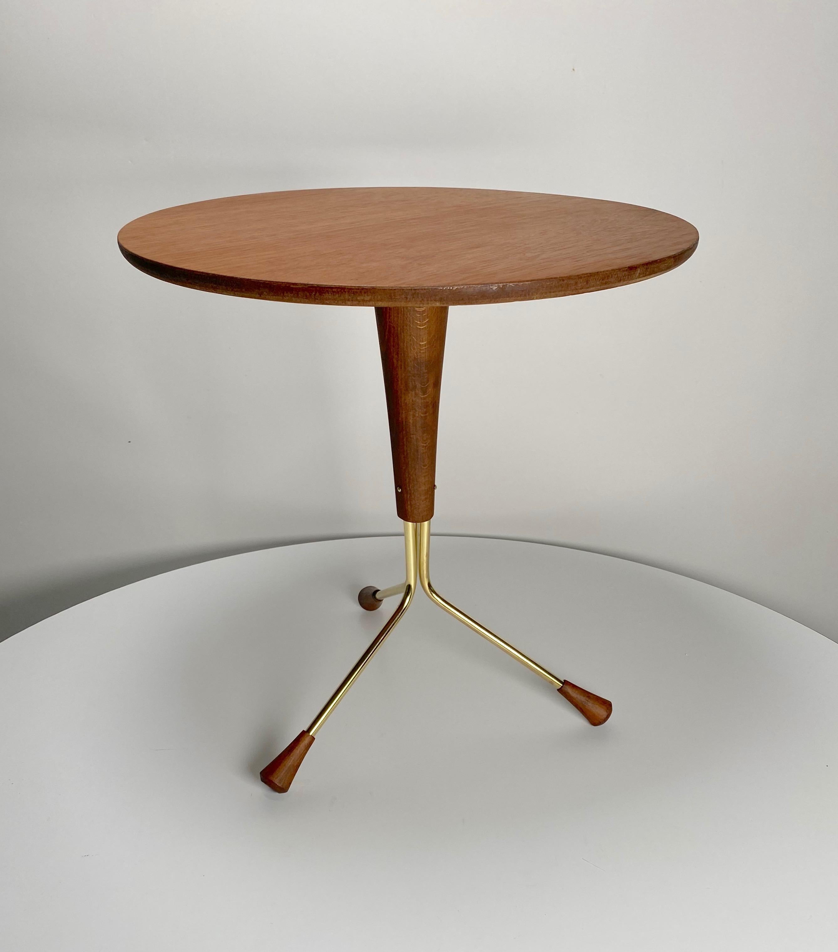 Small tripod base side table in mahogany and brass in the Scandinavian Modern aesthetic by Alberts Larsson for his company Alberts Tibro. Three curved brass legs with turned wooden feet contacted to a tapered wooden base and a round mahogany top.