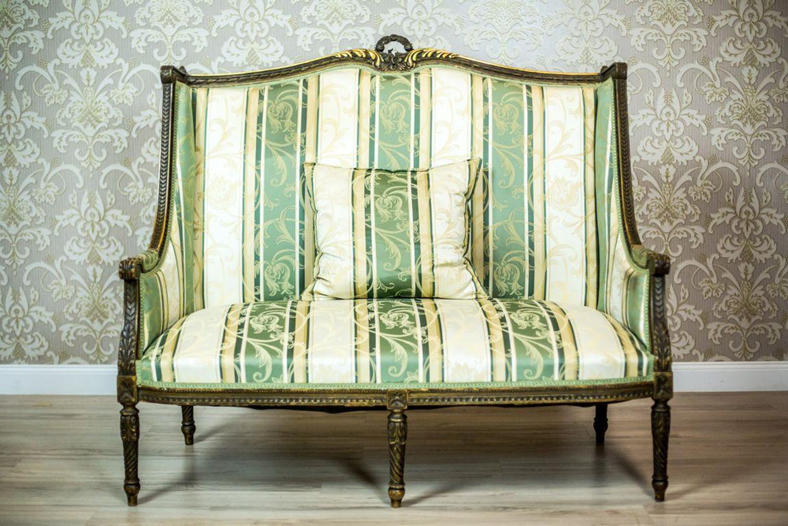 We present you this sofa in the Louis XVI type, two-person, with softly upholstered seat, backrest, and armrests.
The backrest is high, with a wooden topping in the shape of a wreath.
Furthermore, the wooden elements are ornamented with carved