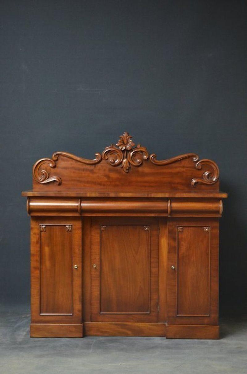 Victorian mahogany sideboard of unusual proportions, having finely carved upstand to back and figured mahogany top over 3 cylindrical drawers and 3 panelled cupboard doors, all enclosing sliders, shelves and deep drawers, all standing on plinth