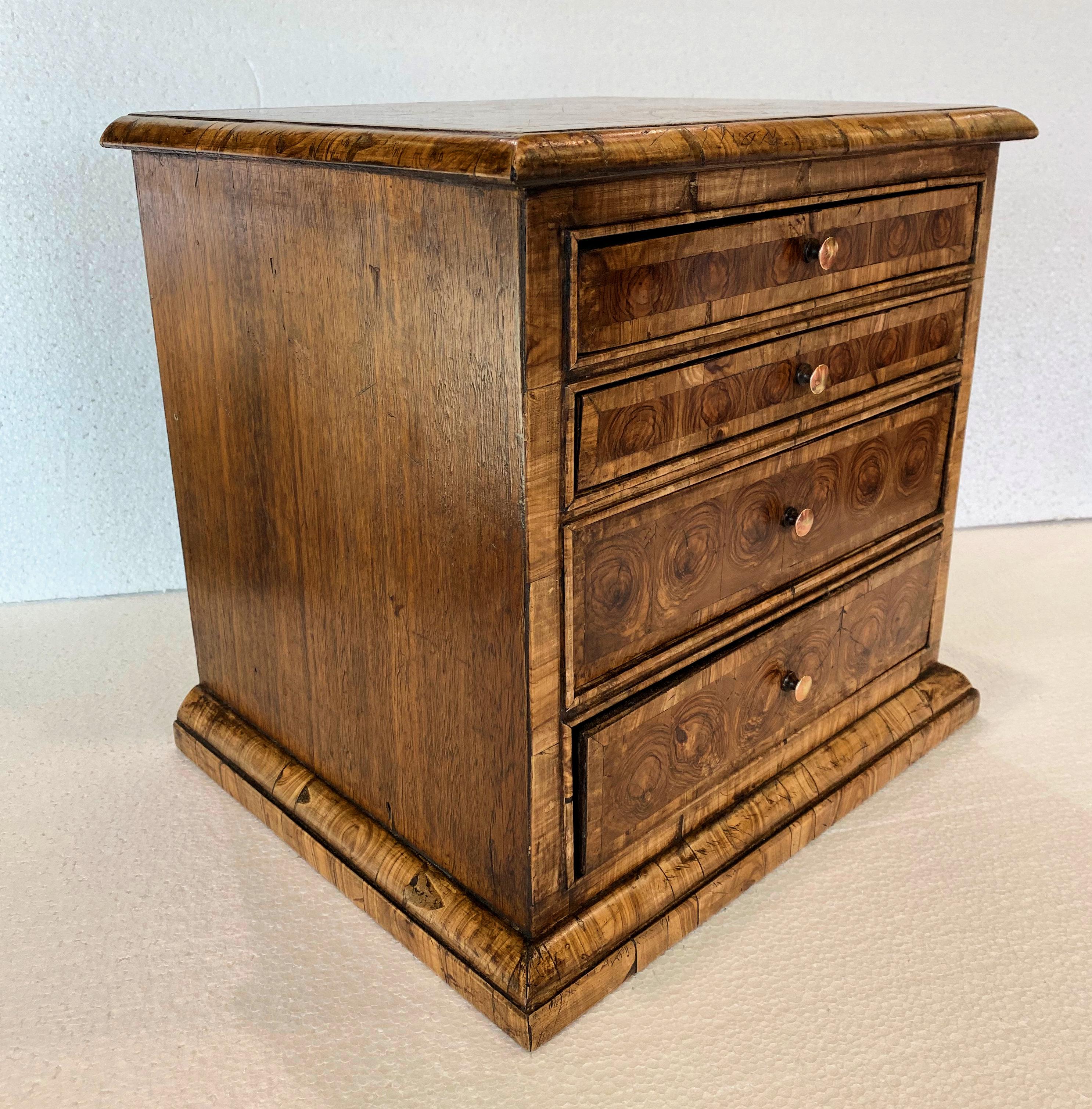 This small Victorian collector's chest has been recently sympathetically re-veneered over the original Victorian oak frame. This lovely chest has 4 graduating drawers with an exquisite olive oyster veneer on the top and drawers. The top features a