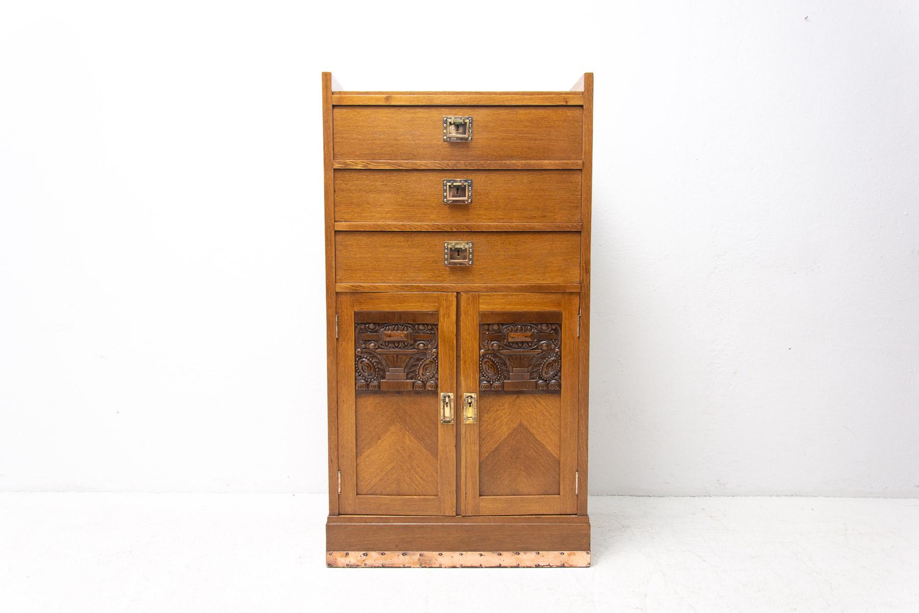 This Secession cabinet was produced in Austria-Hungary, circa 1910. It is made of oak wood and brass. It features three drawers at the top and a storage space at the bottom. It has a beautiful brass fittings with decorative Art Nouveau elements. The