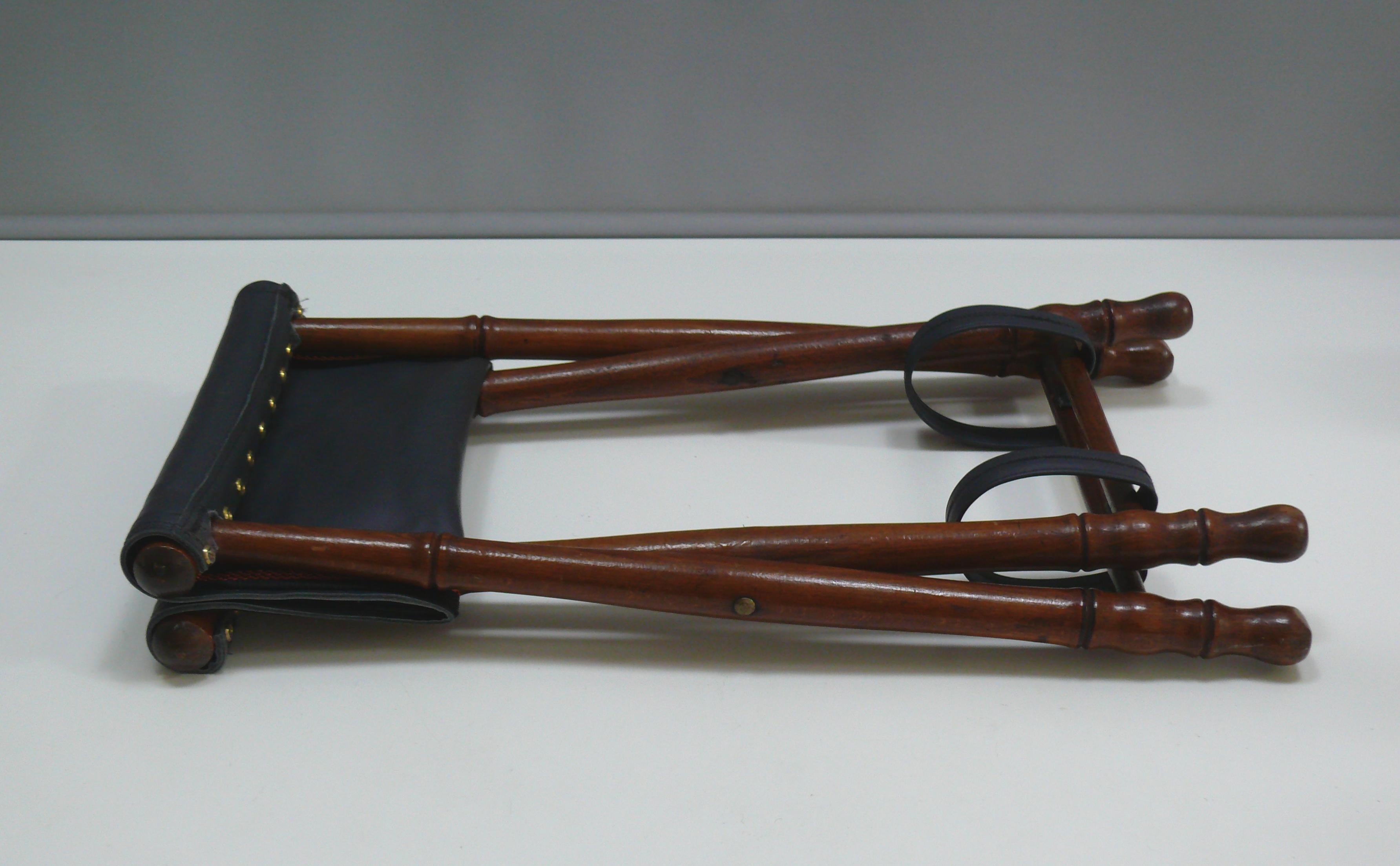 Petit tabouret pliant avec une structure en bois tourné et un siège en cuir véritable (restauré) dans un style colonial, du début au milieu du 20e siècle. Le bois est du teck ou du hêtre teinté et verni sur teck. Le siège mesure 34 x 27 cm et sa