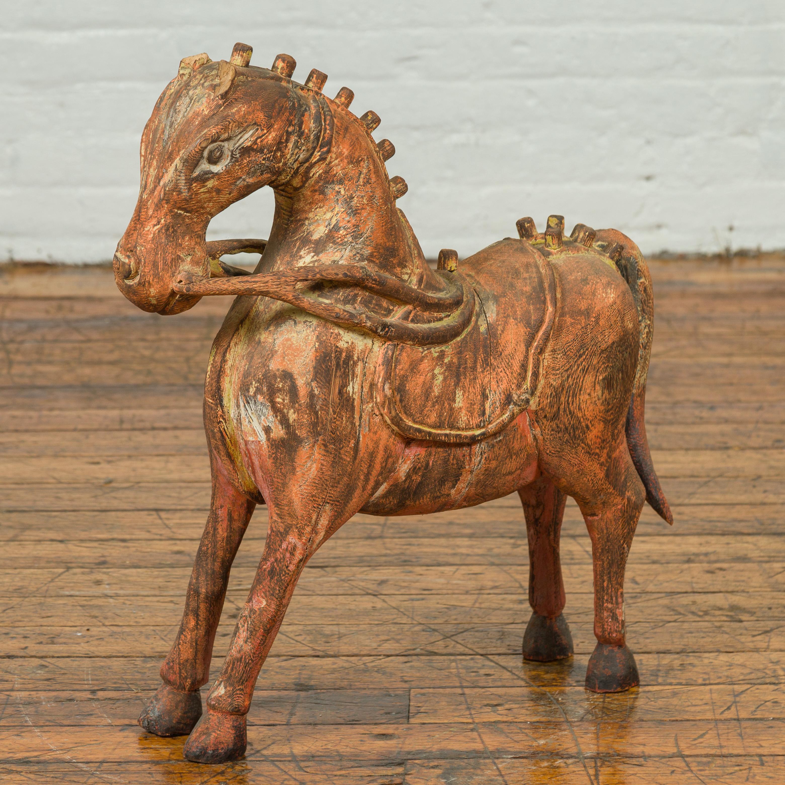 A small Indian vintage carved and rust colored wooden horse sculpture from Madras with distressed patina. Born in the Indian state of Tamil Nadu during the midcentury period, this carved horse charms us with its petite proportions and rust colored