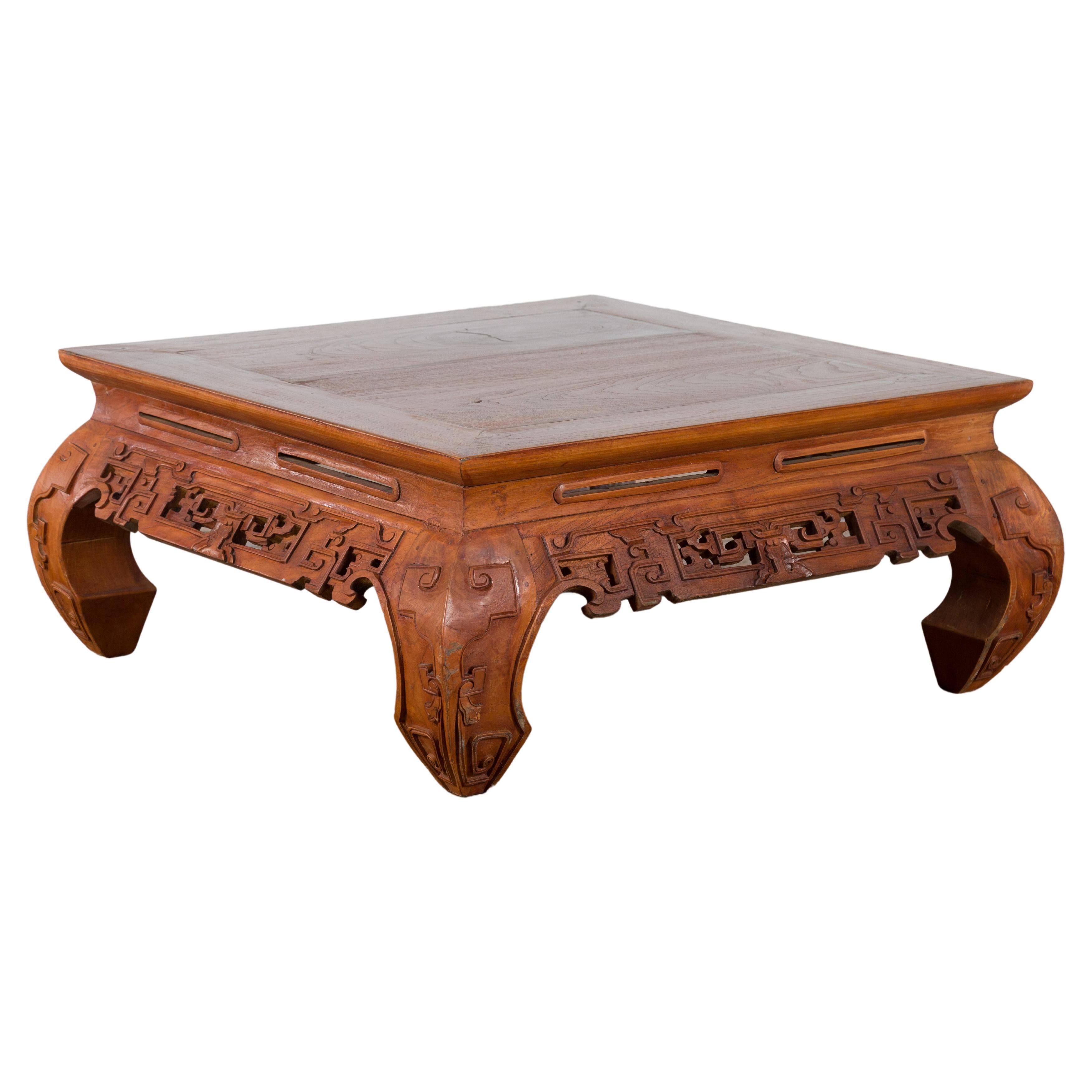 An Indonesian small coffee table from the mid 20th century, with carved apron, chow legs and brown patina. Created in Indonesia during the Midcentury period, this small coffee table features a square top with central board, sitting above an