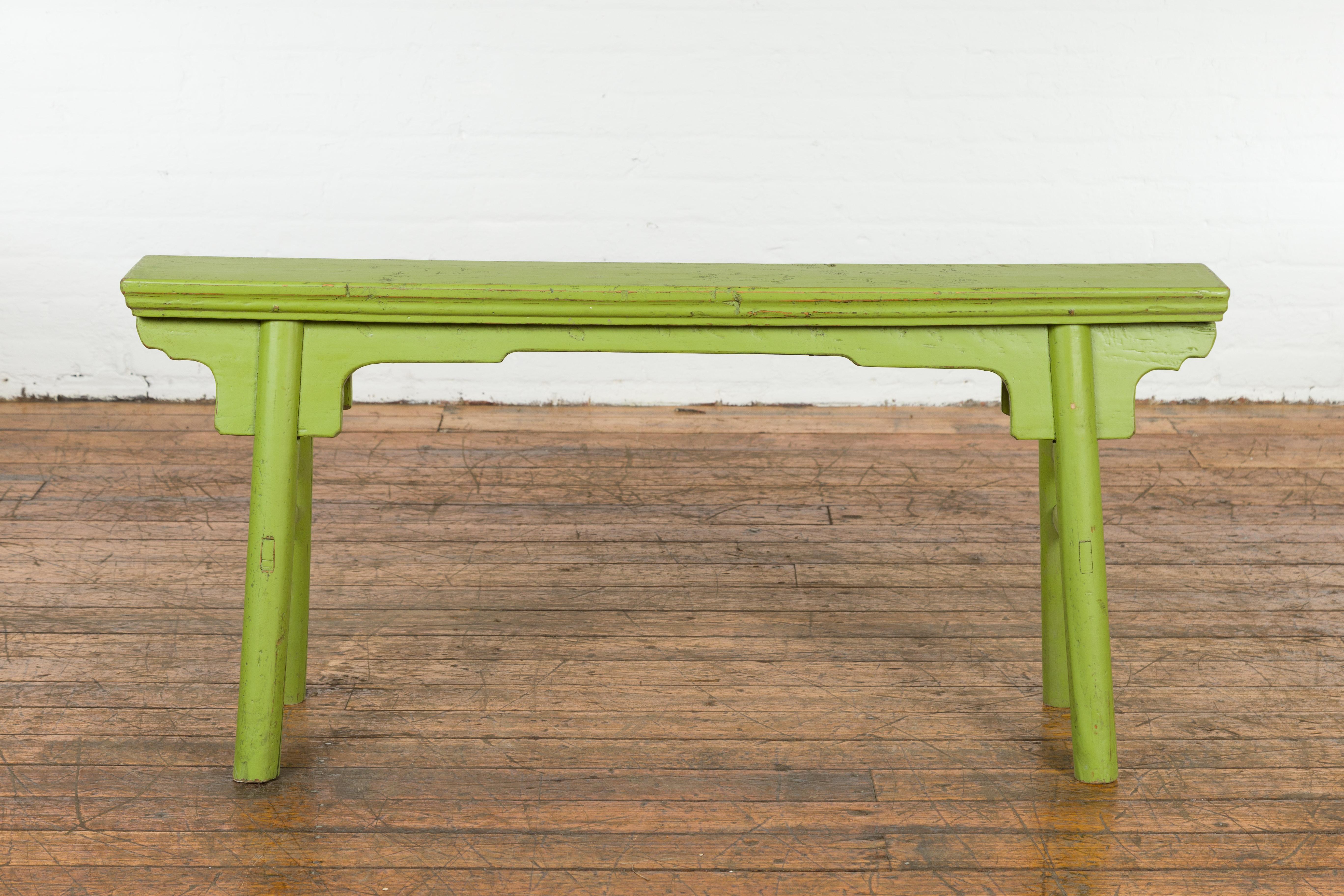 A small vintage Javanese A-Frame wooden bench from the Mid-20th Century, with professionally done custom green painted finish, carved apron and distressed patina. Created in Java during the Midcentury period, this small bench draws the attention