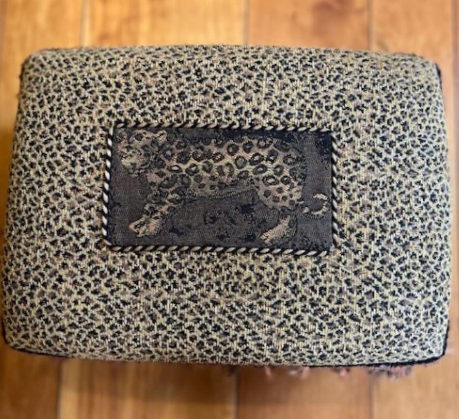 20th c., small leopard print footstool, unmarked, with rope cord, tassel trim and bullion fringe. This small stool has lots of personality and heaps of decorative elements. The leopard print fabric frames a depiction of a leopard on the seat of the